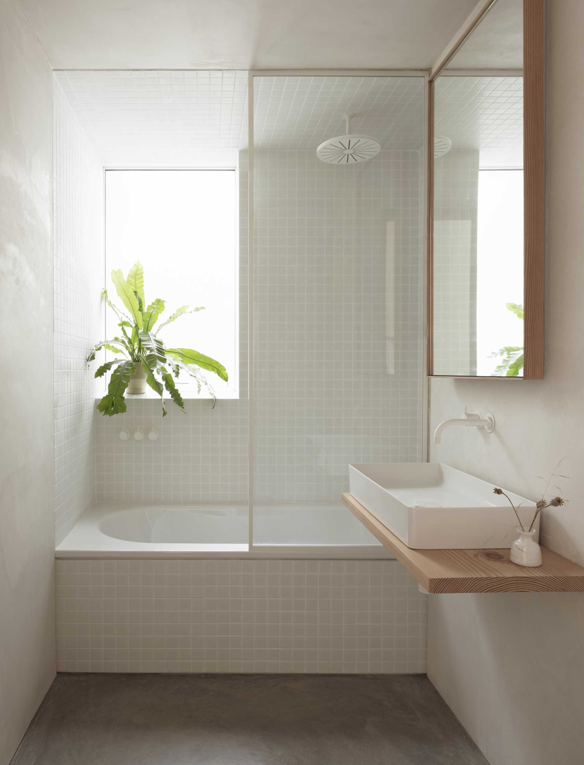 In this modern bathroom, small square tiles cover the walls and ceiling in the bath / shower area, while wood has been used as an accent material around the mirror and as the vanity.