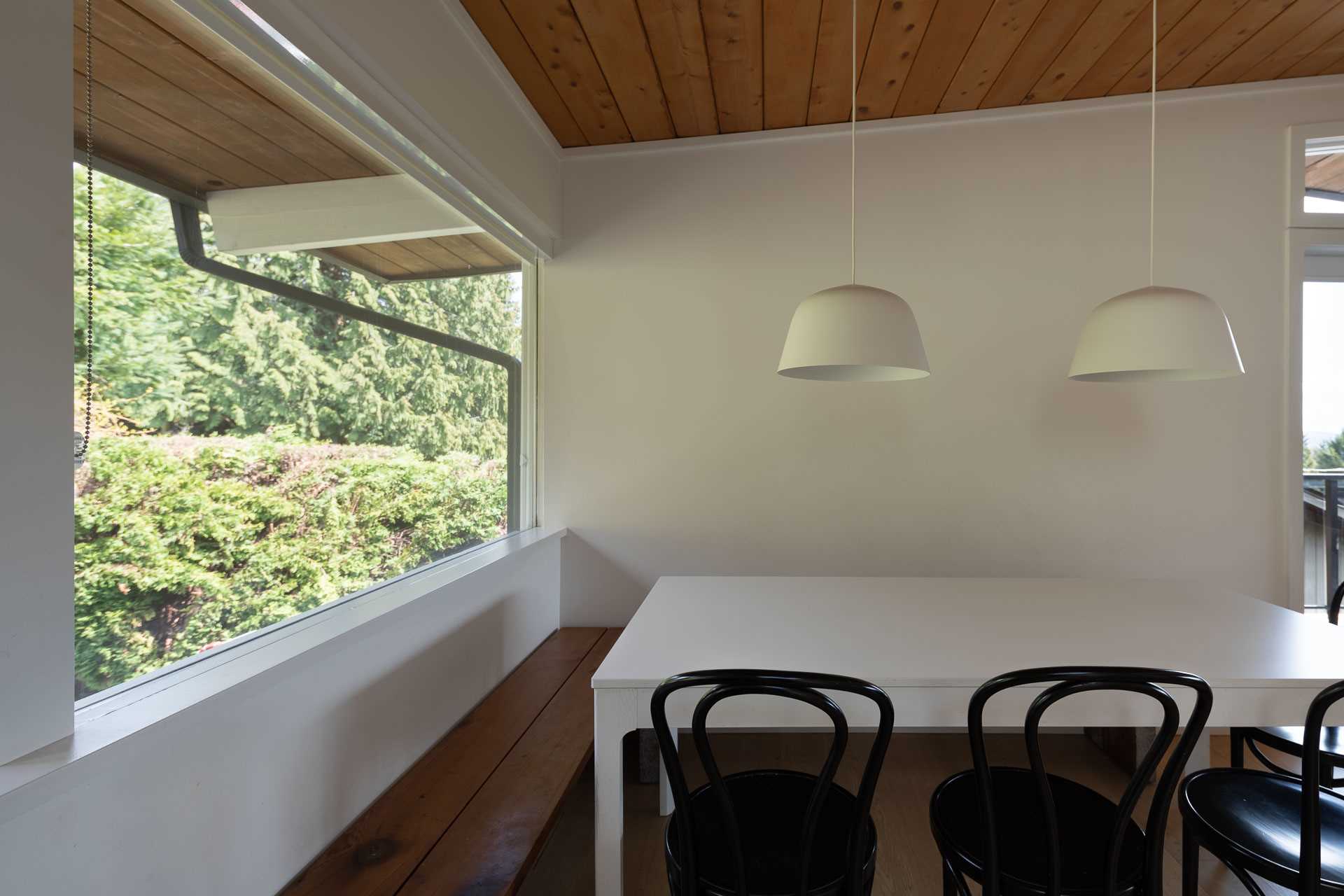 This newly remodeled dining room is open to the living room and kitchen, and now includes two minimalist white pendant lights hanging above a simple white table.