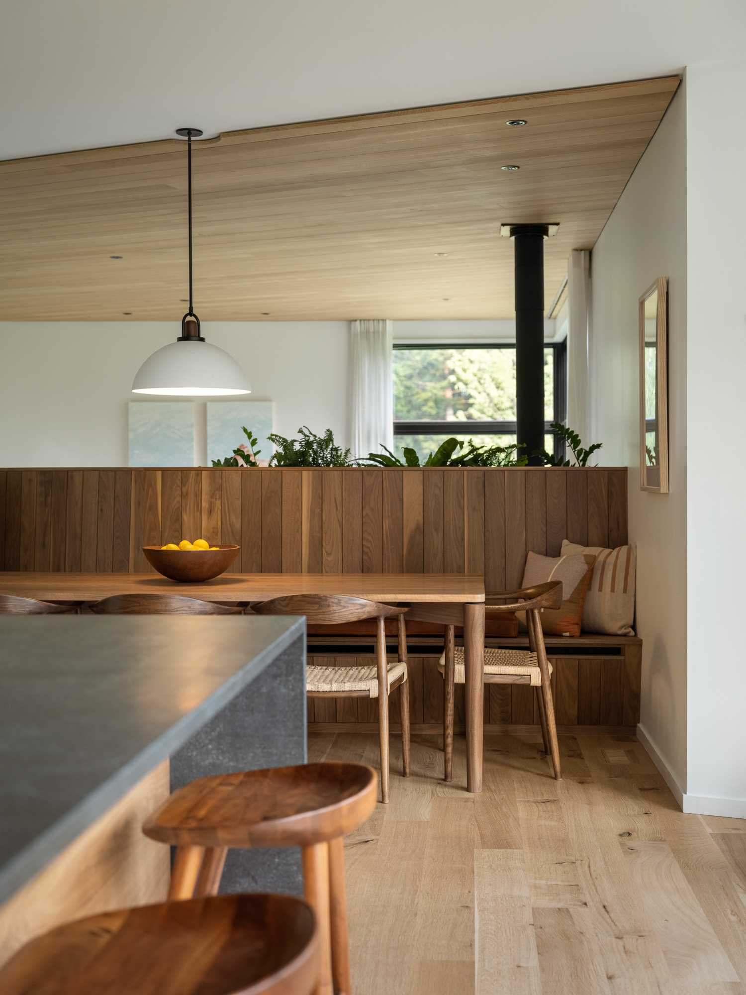 The dining room has a unique design, with a sculptural wood banquette bench that acts as seating for the table.
