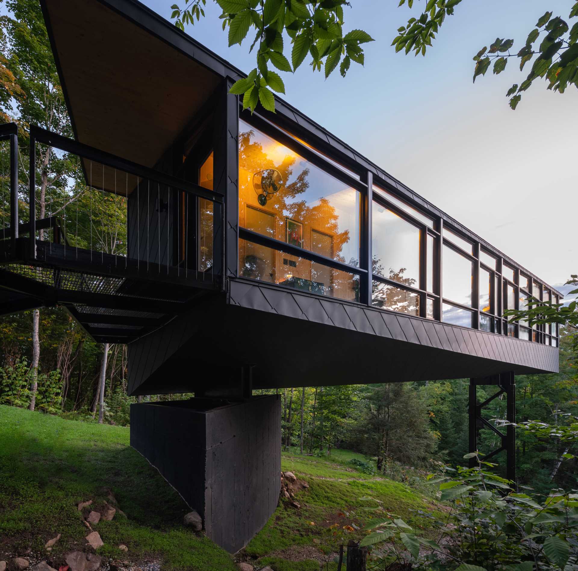 A black cabin that's elevated and has a wall of windows.