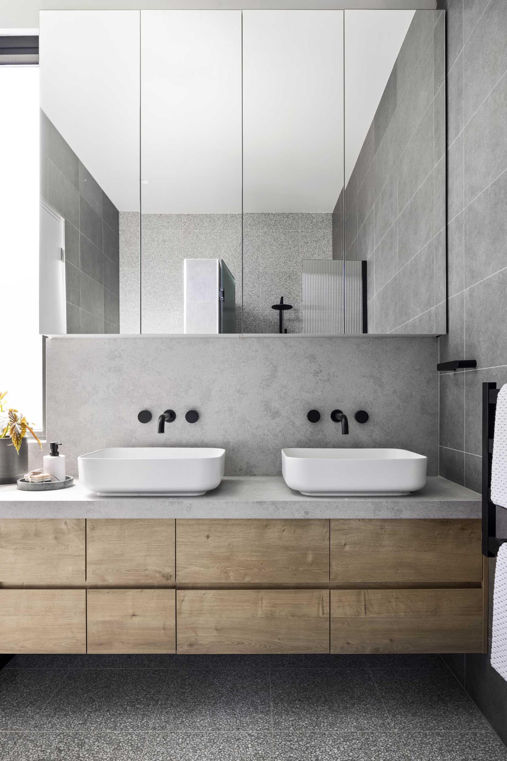 In this modern bathroom, there's Terrazzo tile flooring, a wood vanity, and black tapware and fixtures.