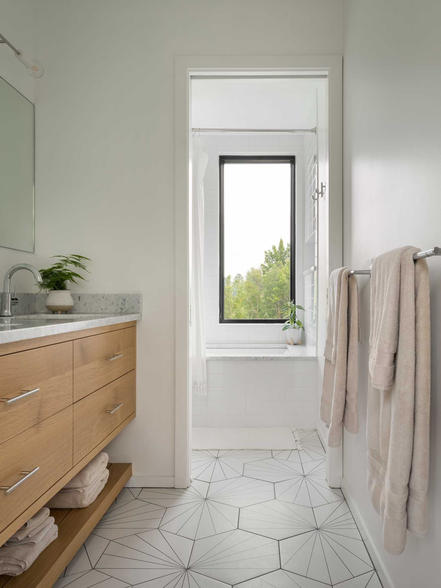 A modern bathroom with white walls, wood vanity, and light starburst tile flooring.