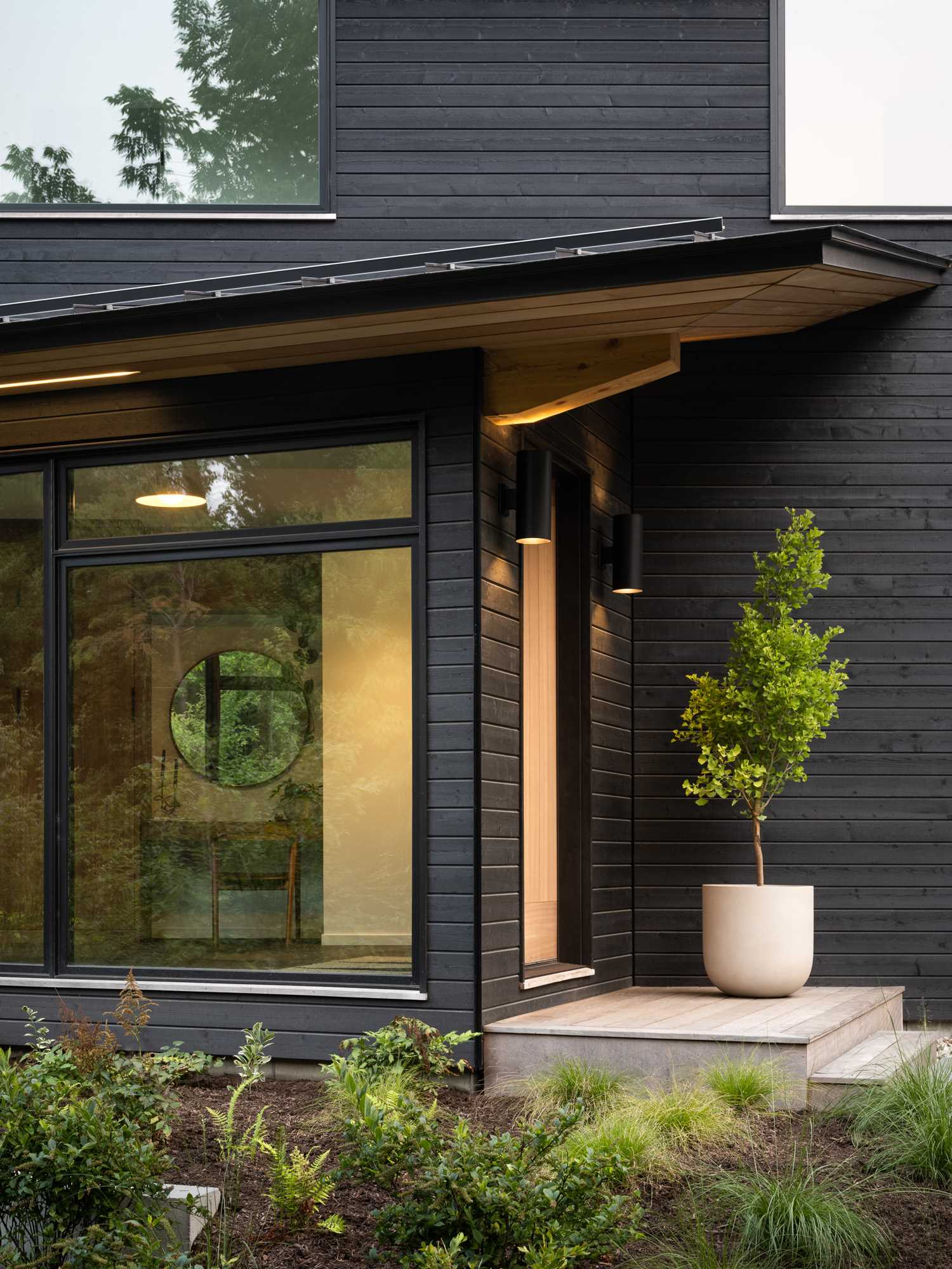 Lighting on either side of the front door welcomes people to this modern home with black stained wood siding.