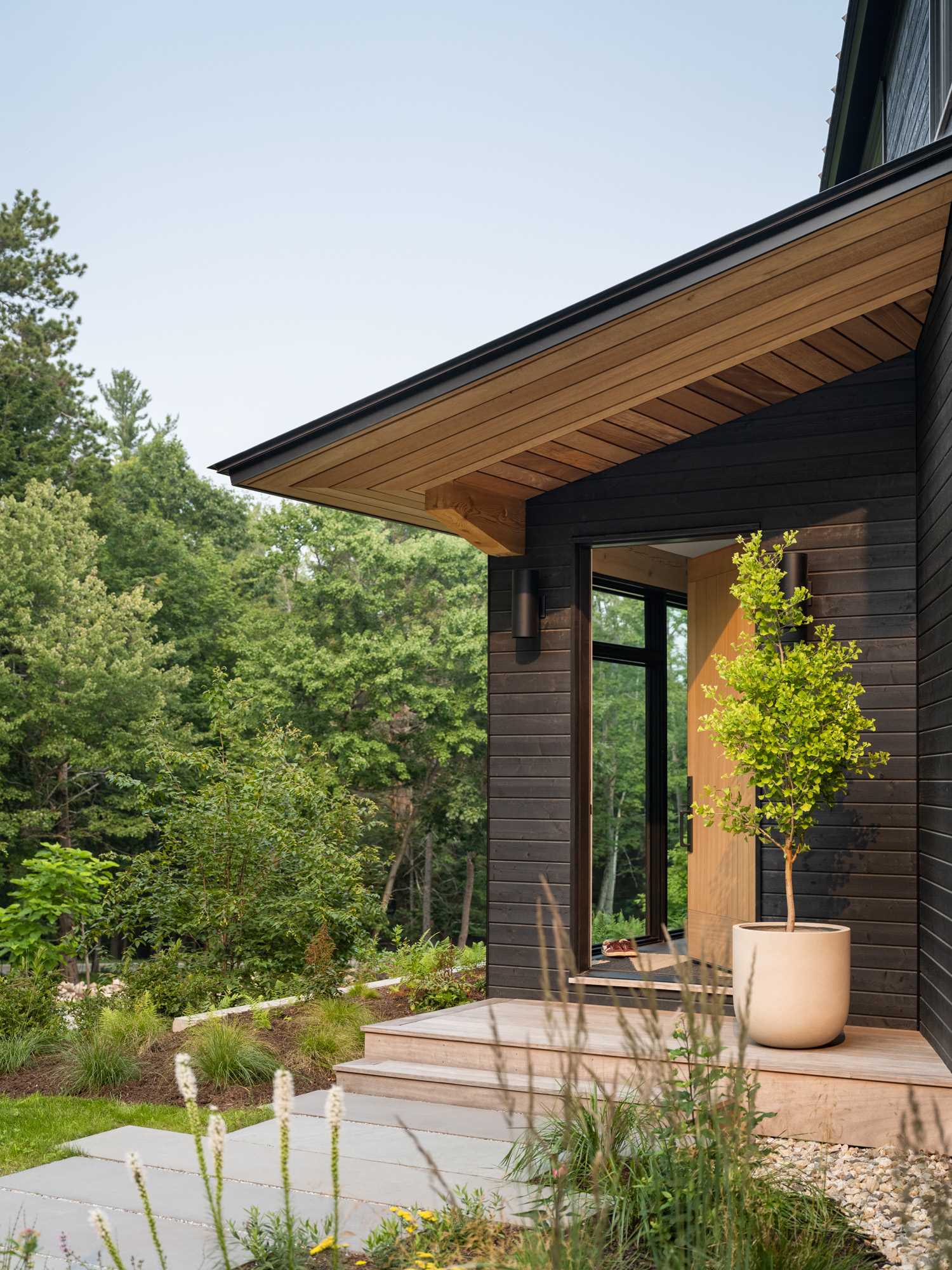 Lighting on either side of the front door welcomes people to this modern home with black stained wood siding.
