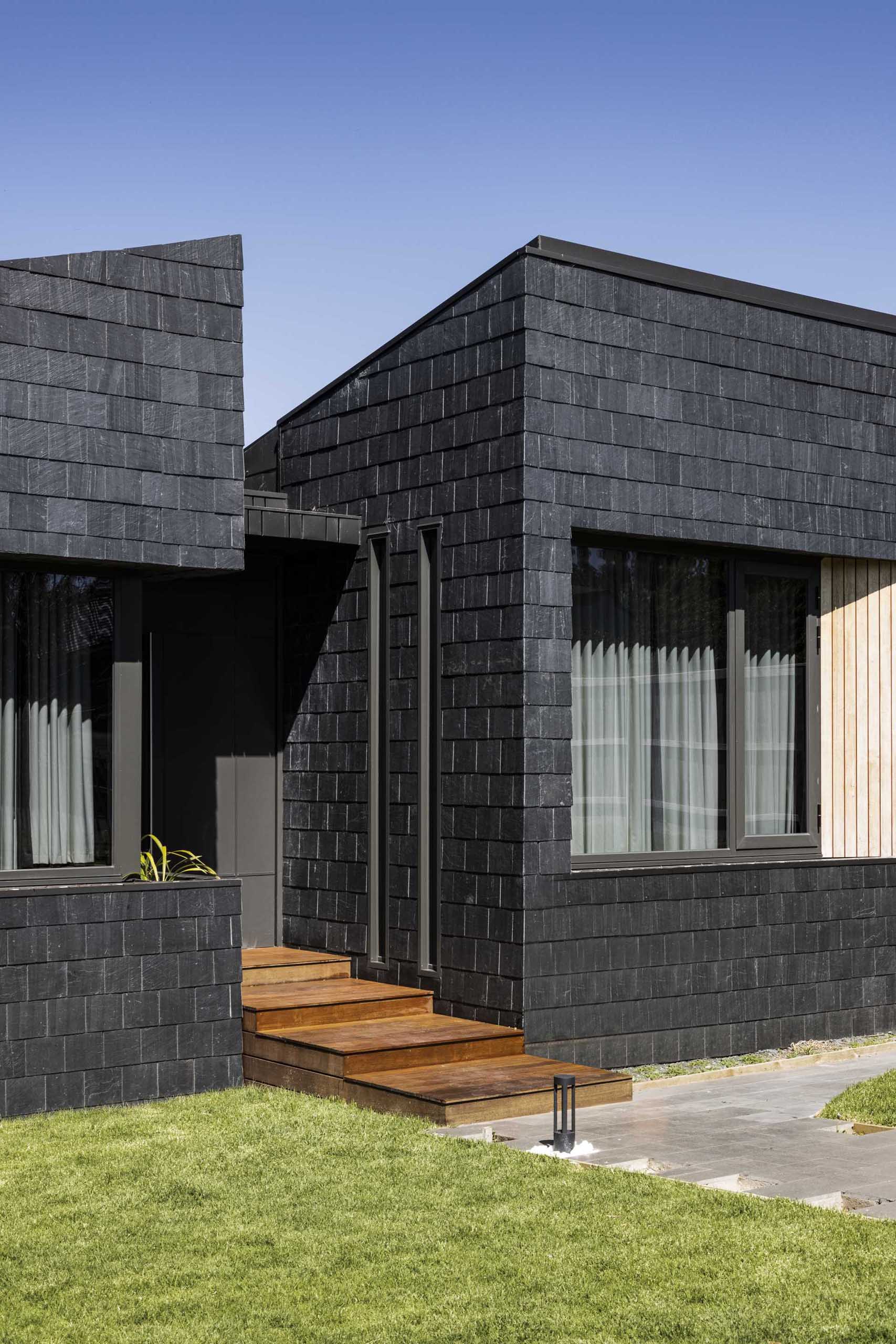 A modern house clad in black slate shingles and wood accents.