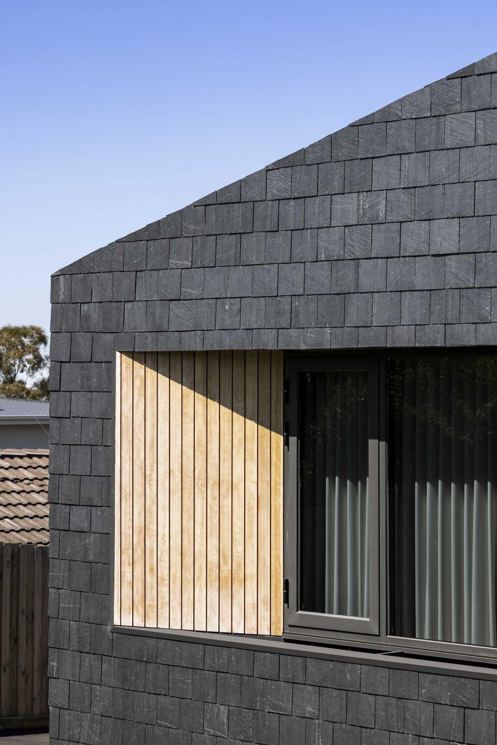 A modern house clad in black slate shingles, wood accents, and charcoal window frames.