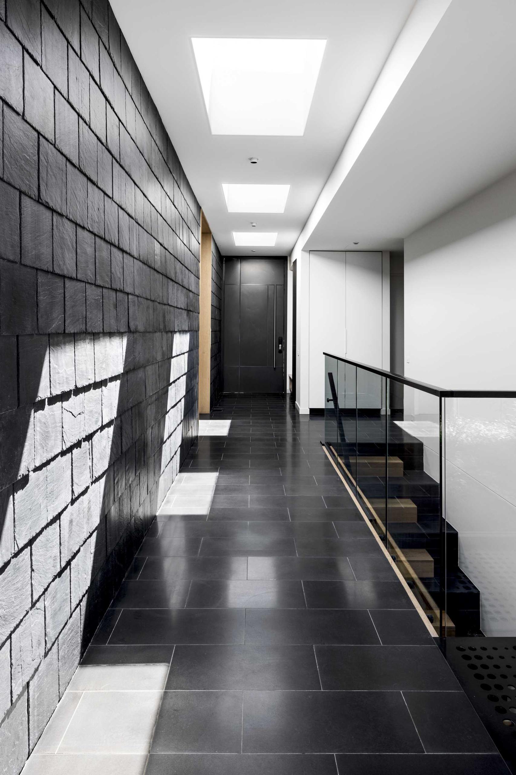 A modern hallway with textured black slate shingles and black tile flooring.
