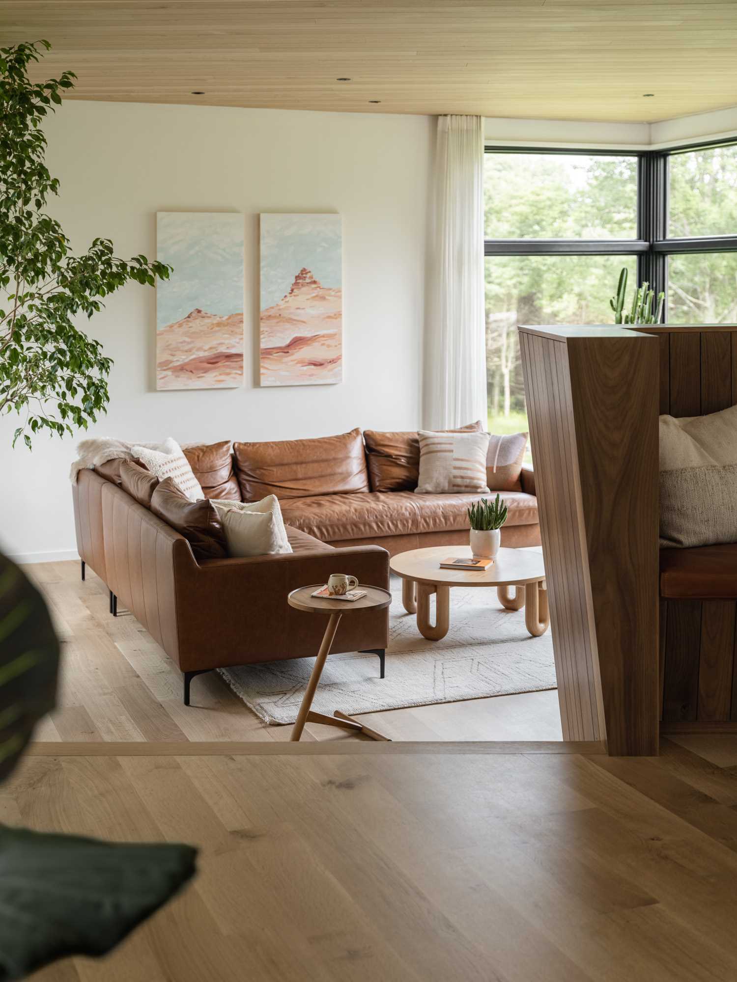 In this modern living room, there's a wood ceiling, large brown leather couch, and a few plants.