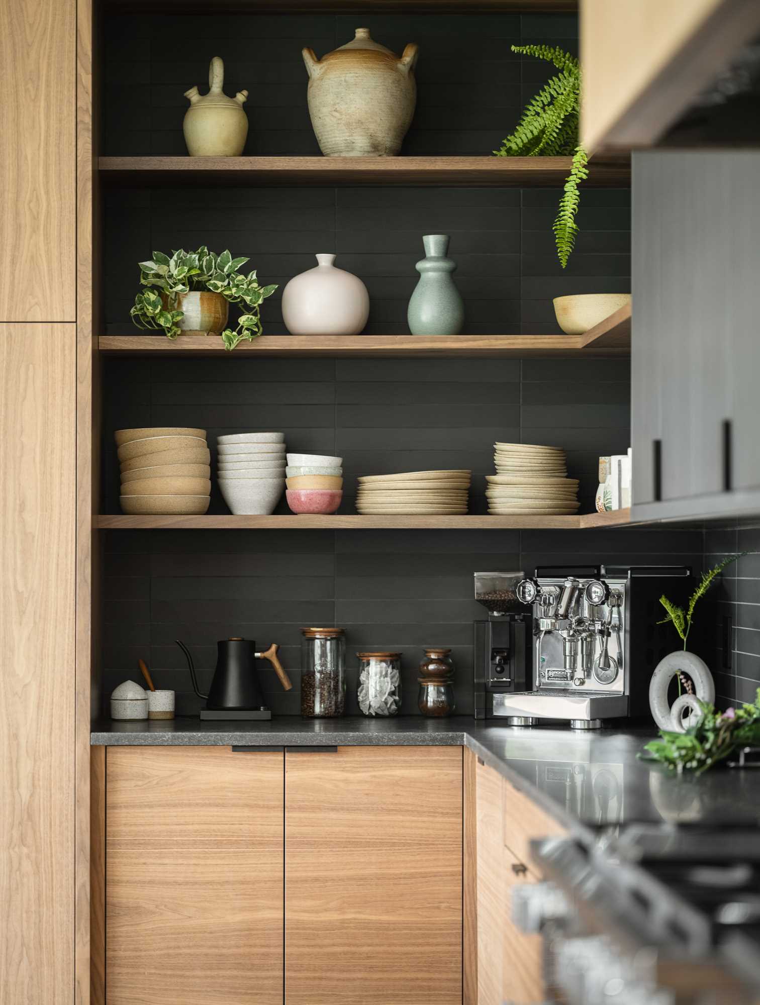 A modern kitchen with wood cabinets, open corner shelves, and black rectangular tiles.