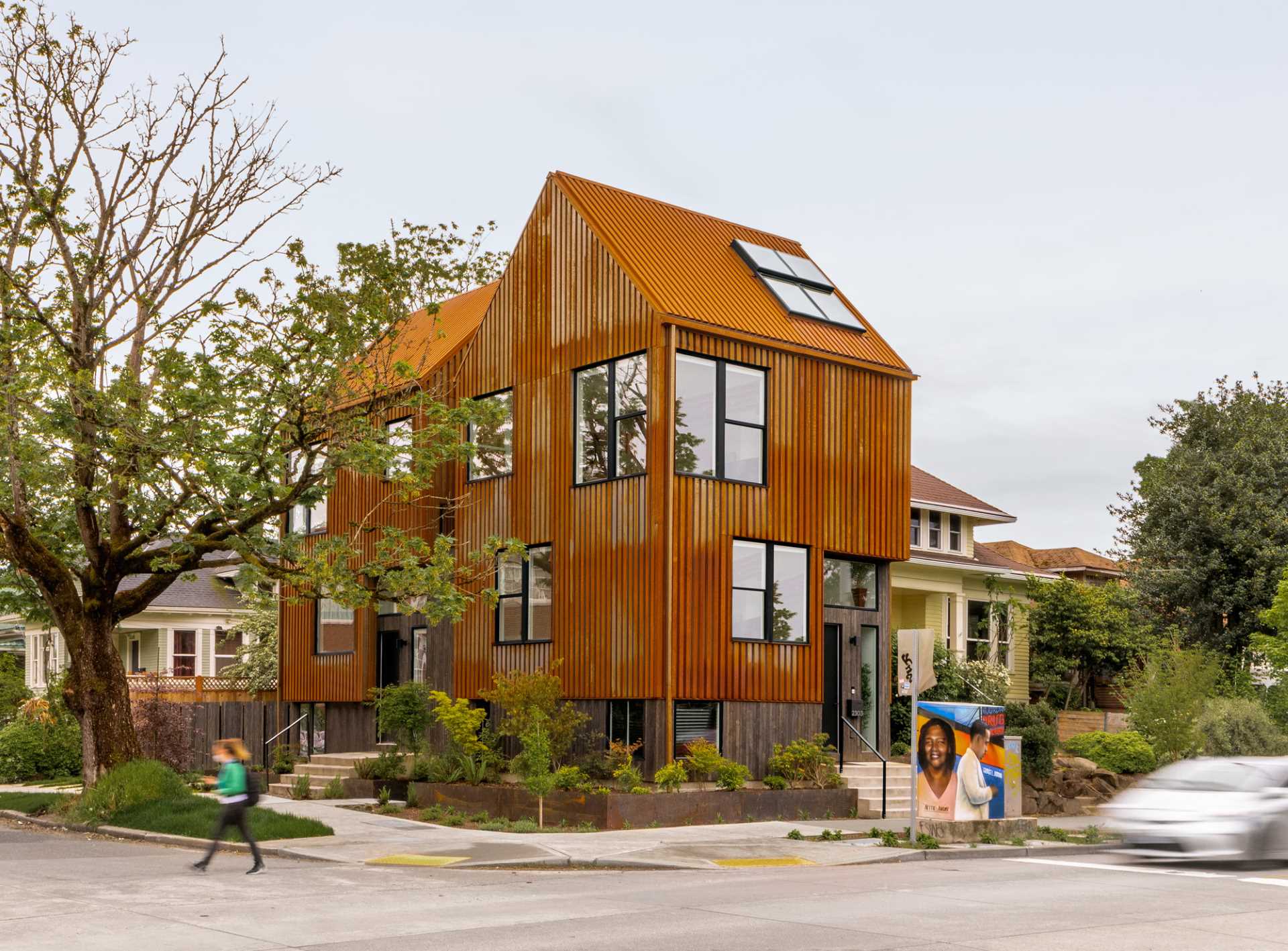 A modern townhouse on a corner, has an exterior clad in rusted corten steel.