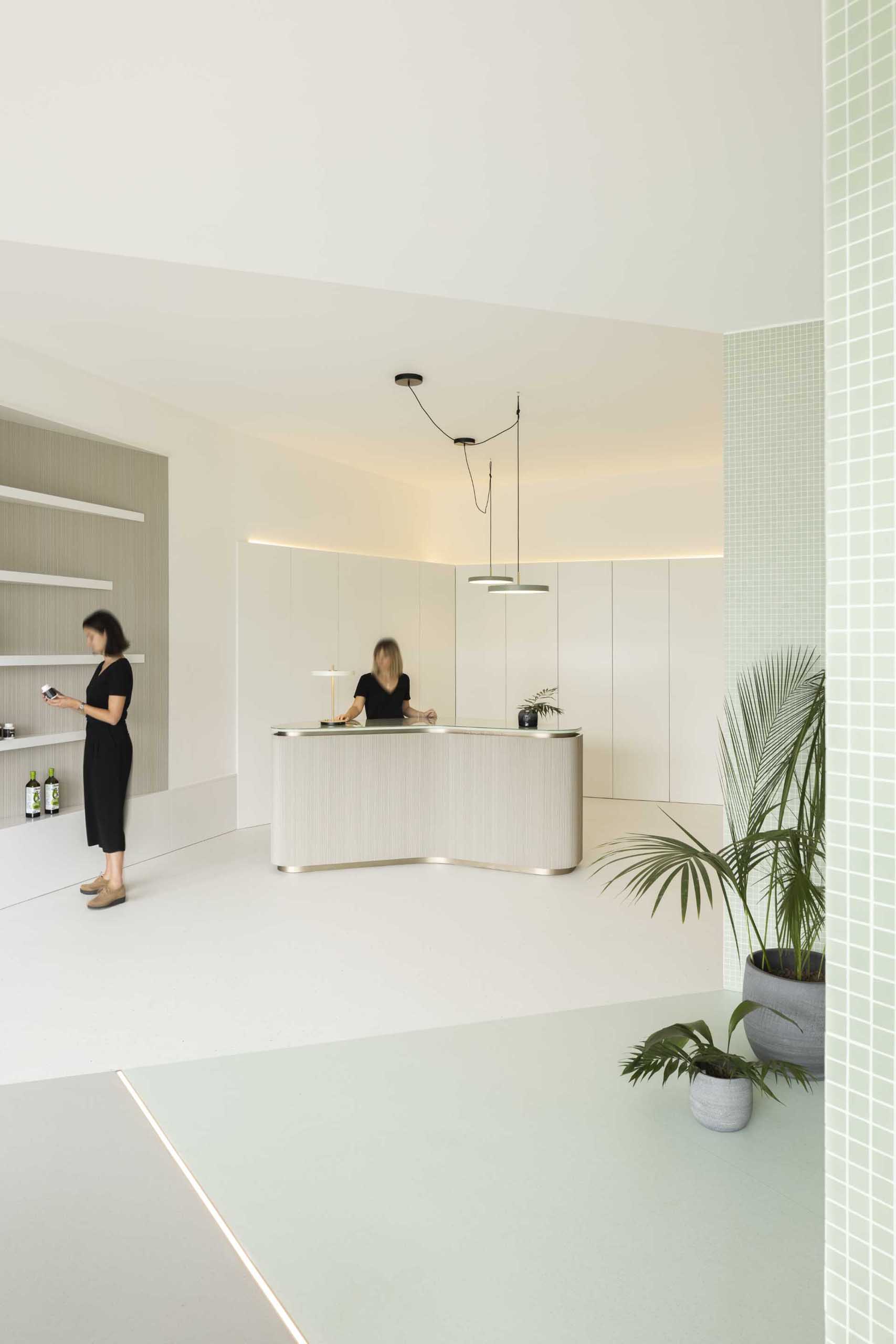 The minimalist reception area of this health clinic is split into two spaces, the first includes a curved desk and wall shelf, the second, which is in pastel green, is dedicated to a waiting area and office.