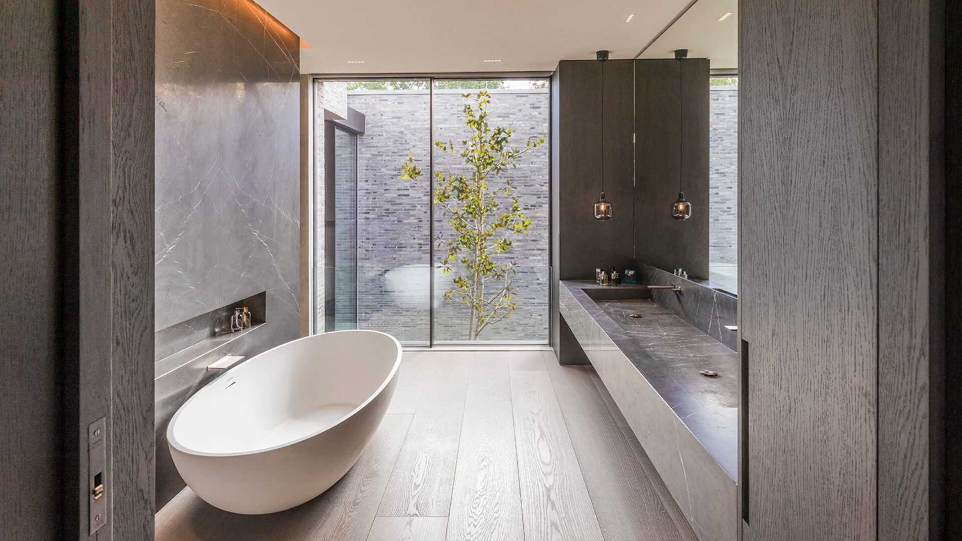 In this modern bathroom, a freestanding bathtub sits beside a shelving niche, while the windows provide a view of the grey brickwork.