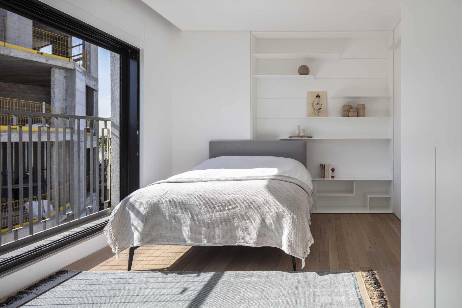 A minimalist white bedroom with wood floors and thin shelving.