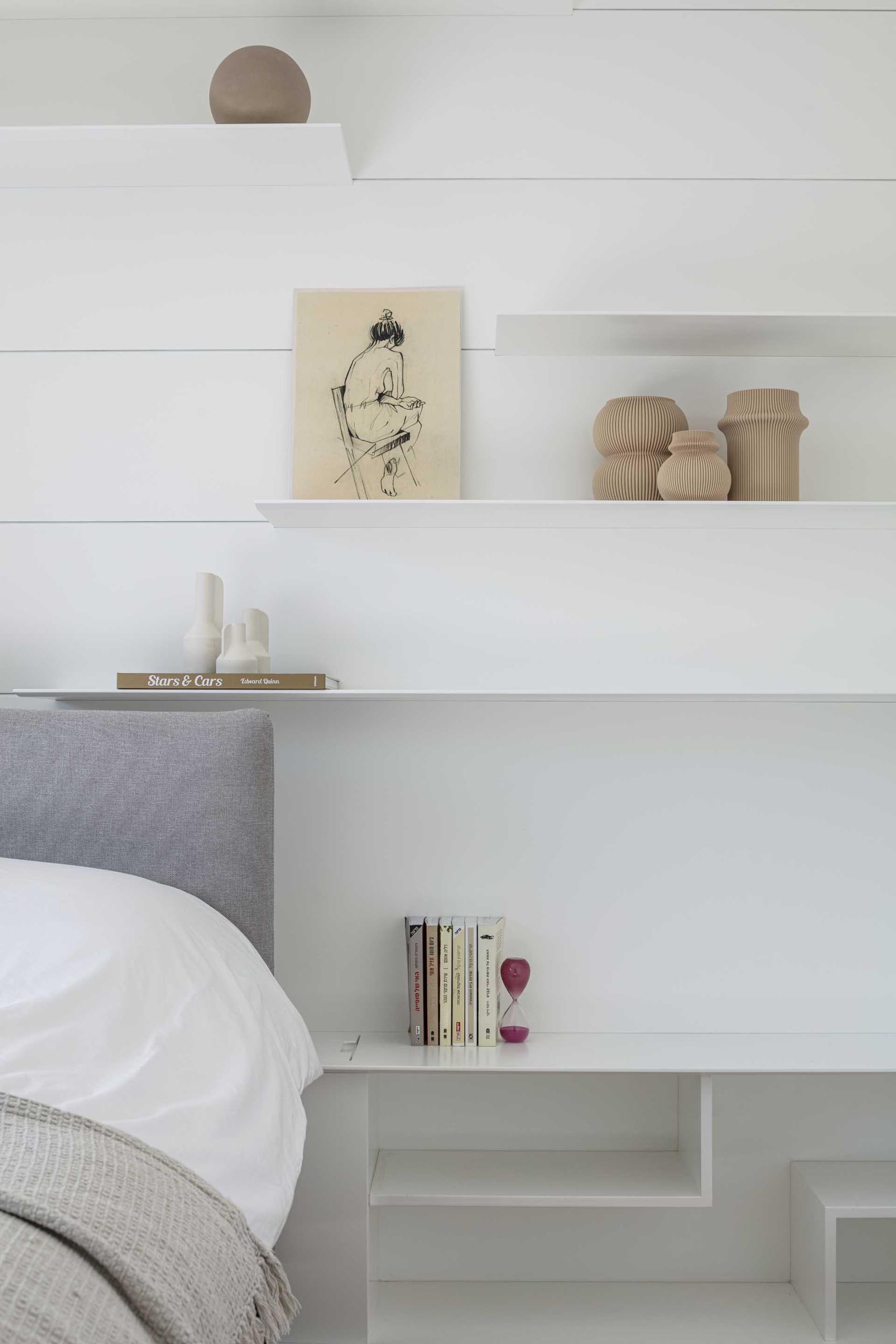 A minimalist white bedroom with wood floors and thin shelving.