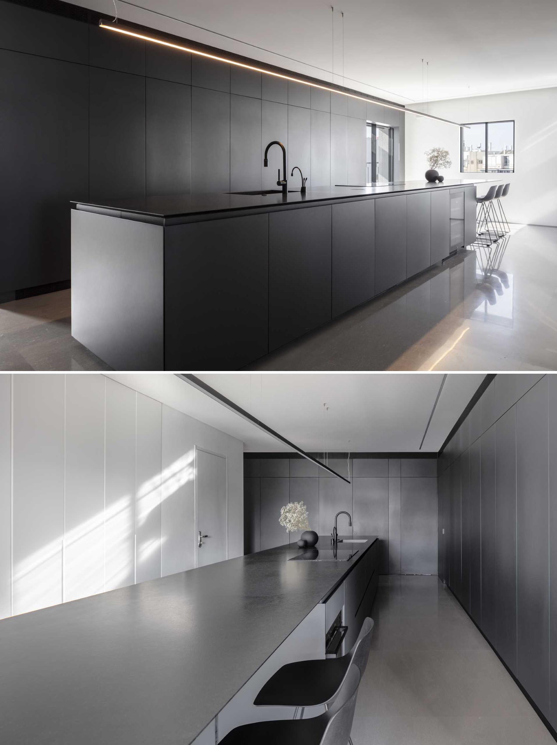 In this modern kitchen, minimalist cabinets in a shade of graphite and white line the wall, while the island is covered with black granite and extends to include space for seating.