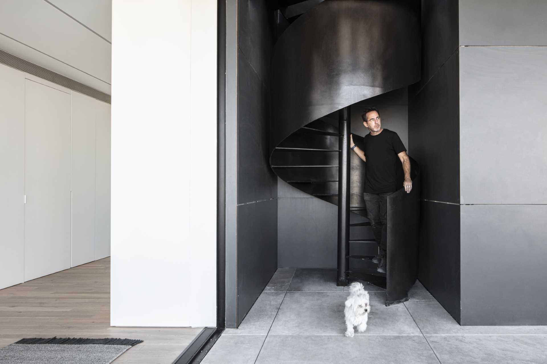 A modern penthouse apartment has black spiral stairs that lead to the rooftop.