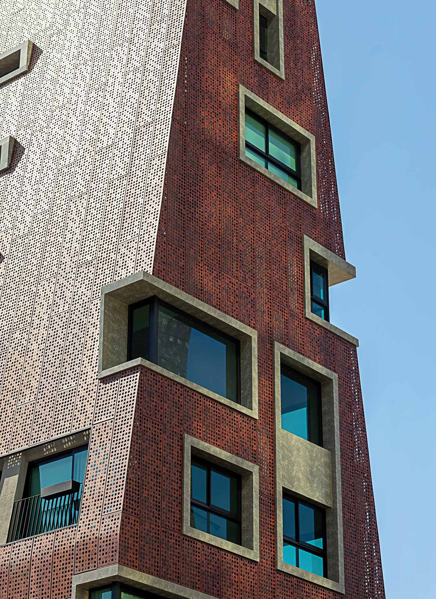 The facade that covers this modern building is made from perforated aluminum panels, each painted in an earthy reddish sepia tone.