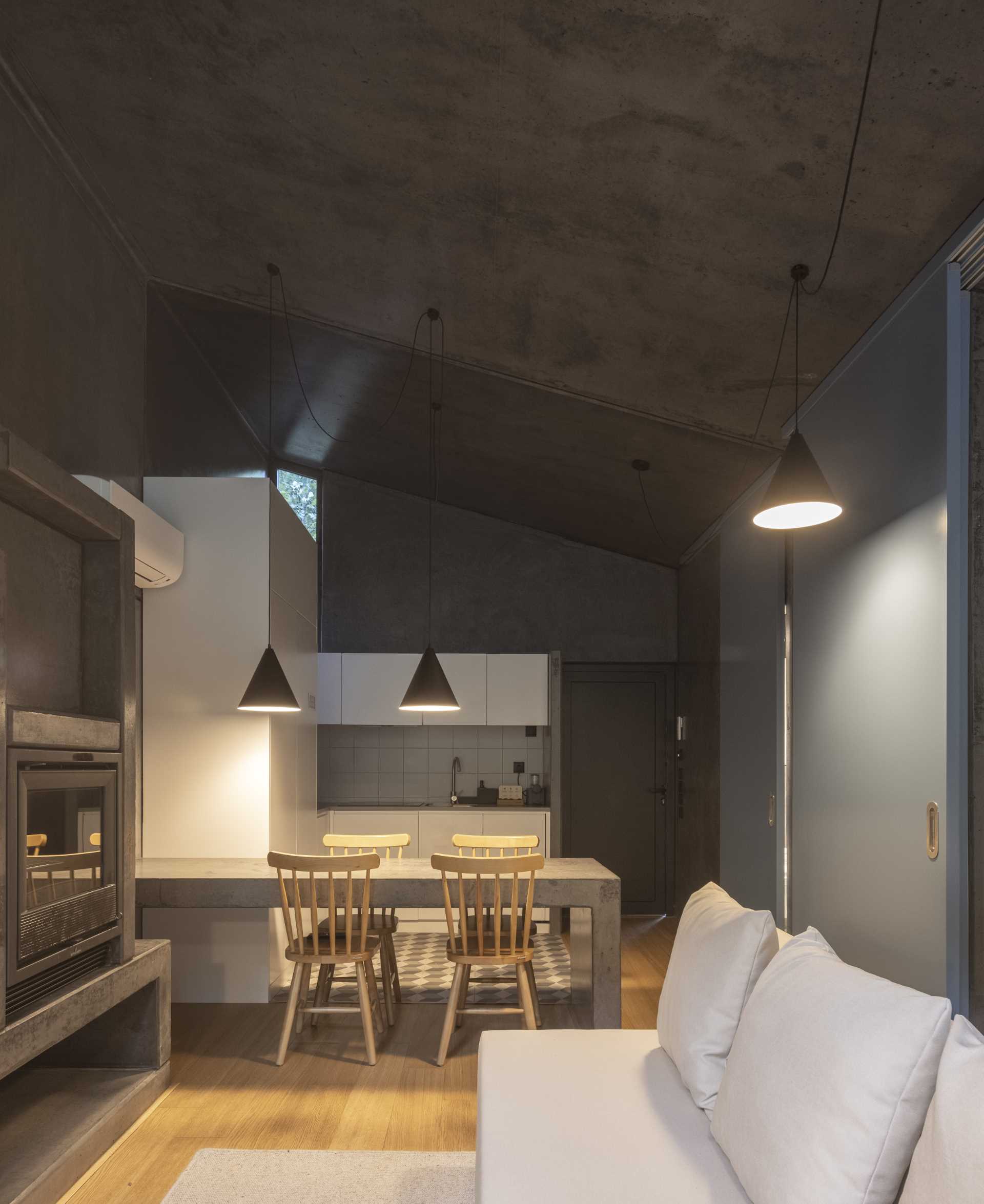 A small home with raw concrete walls, wood floors, a built-in dining table, and fireplace