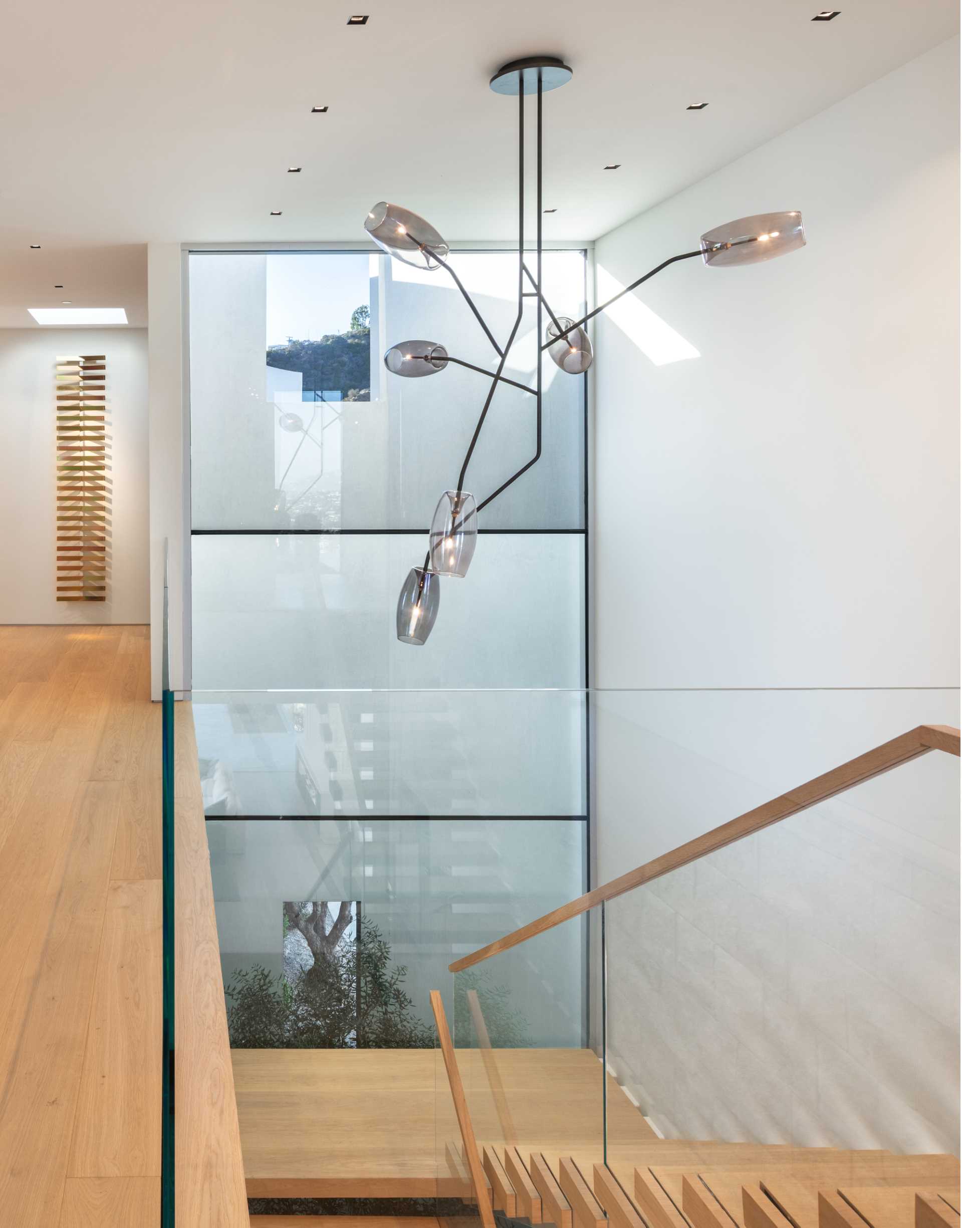 Stairs with a glass and wood handrail connect the various levels of this modern home, while a sculptural light fixture adds interest to the space.