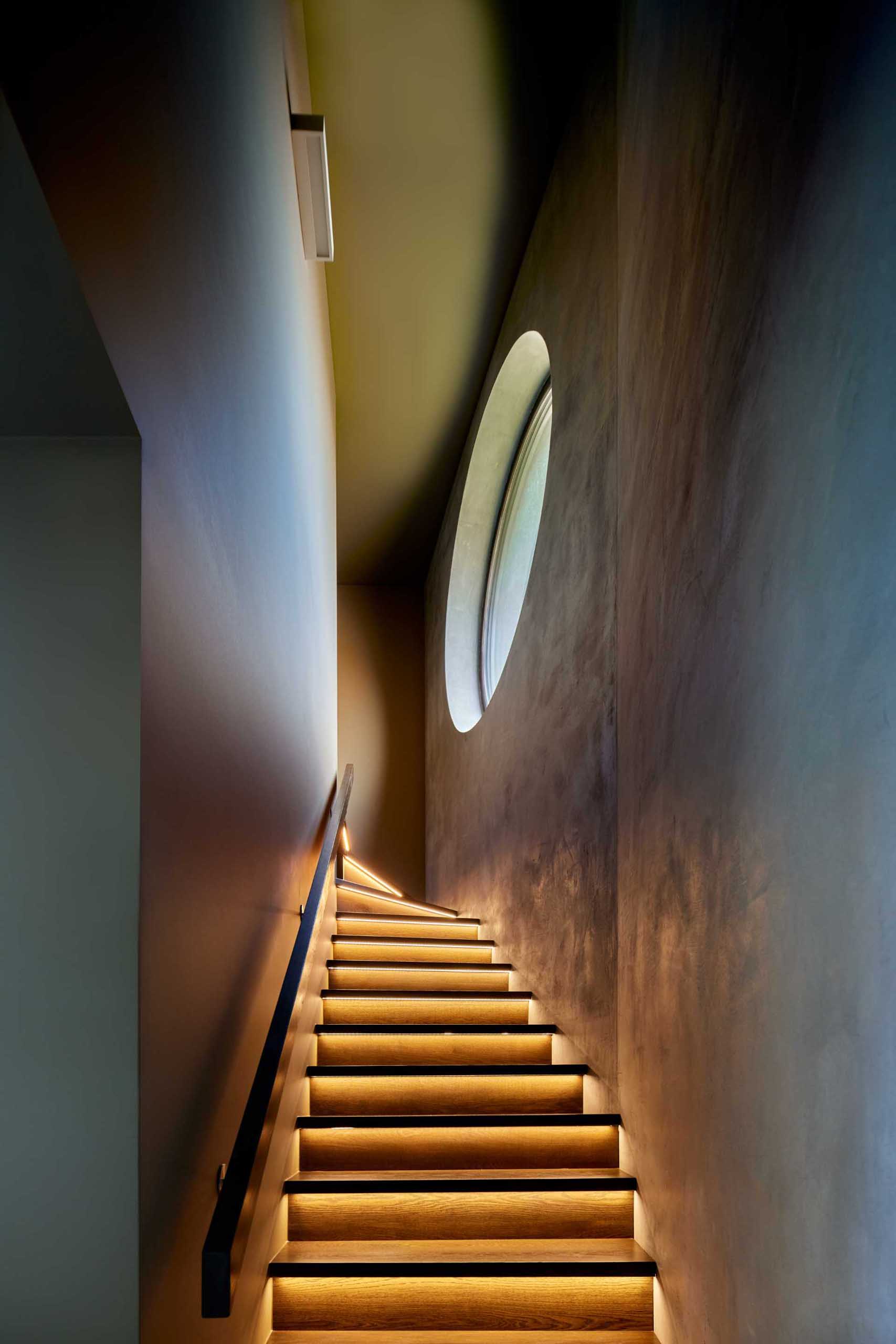 This modern and dark staircase includes hidden LED lighting underneath each stair tread, while the round window adds natural light during the day.