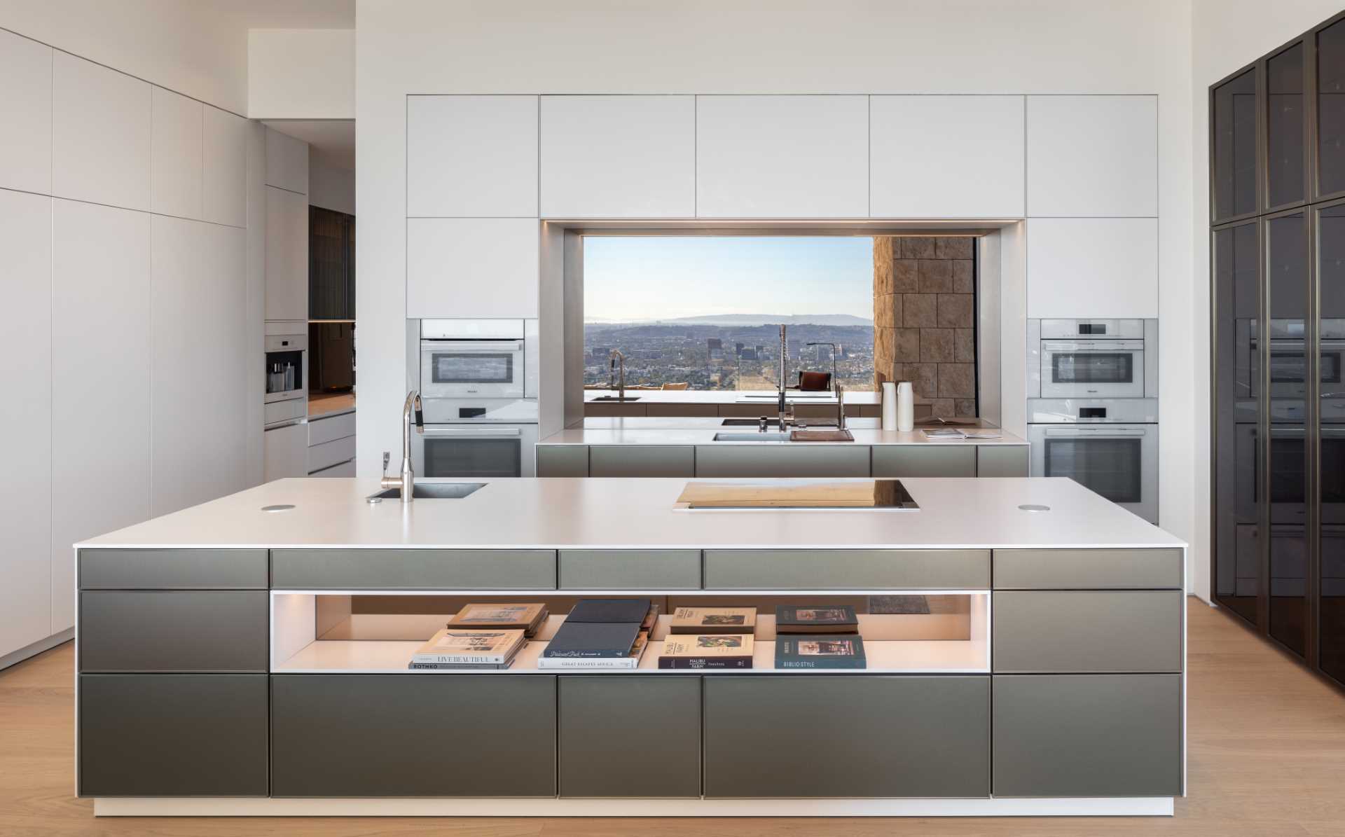 This modern kitchen has minimalist white cabinets that sit flush with the walls, while a large island includes a shelf with a mirror for displaying books.