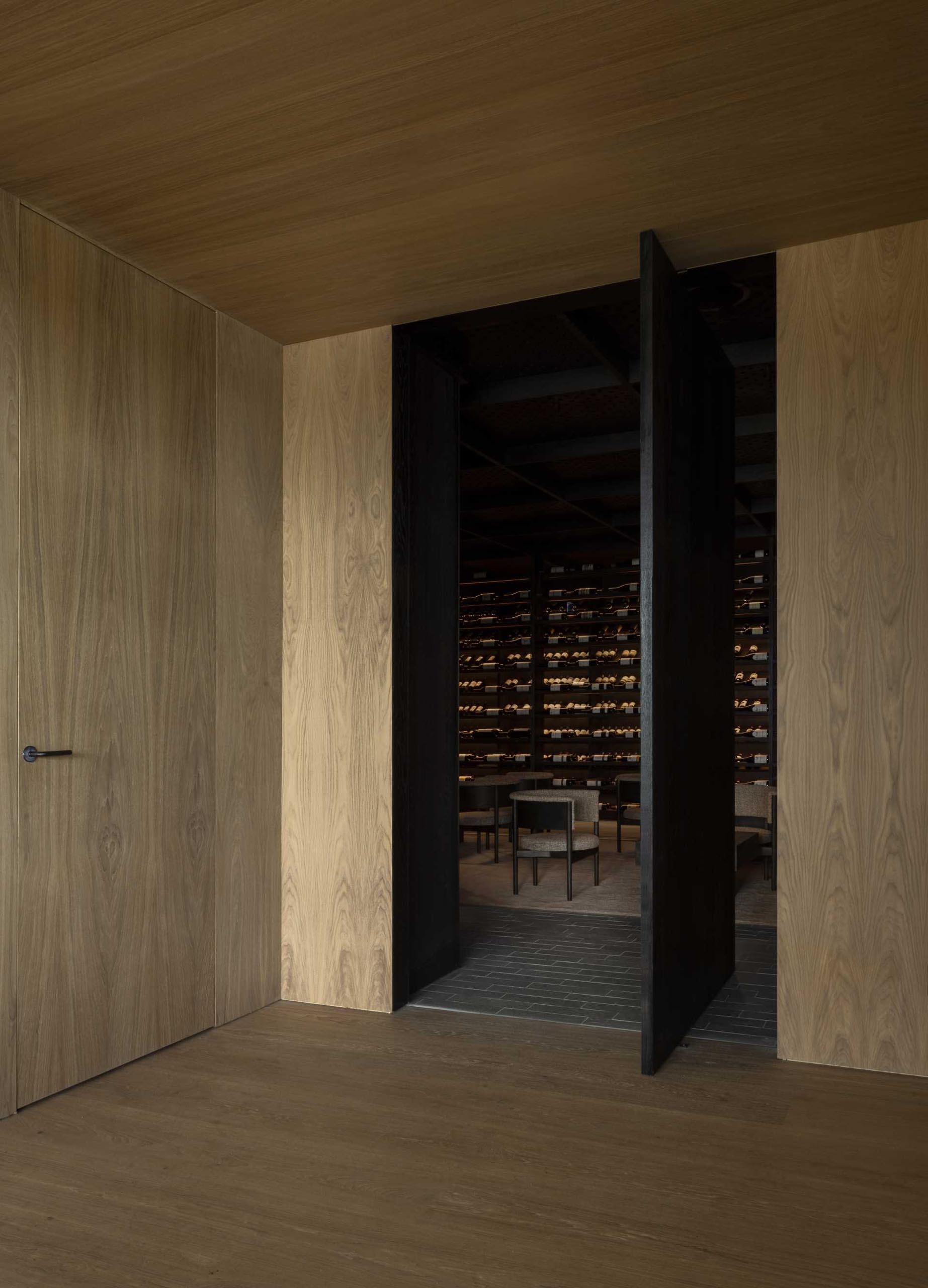 An oversized pivoting door opens to reveal a dark and moody wine cellar.
