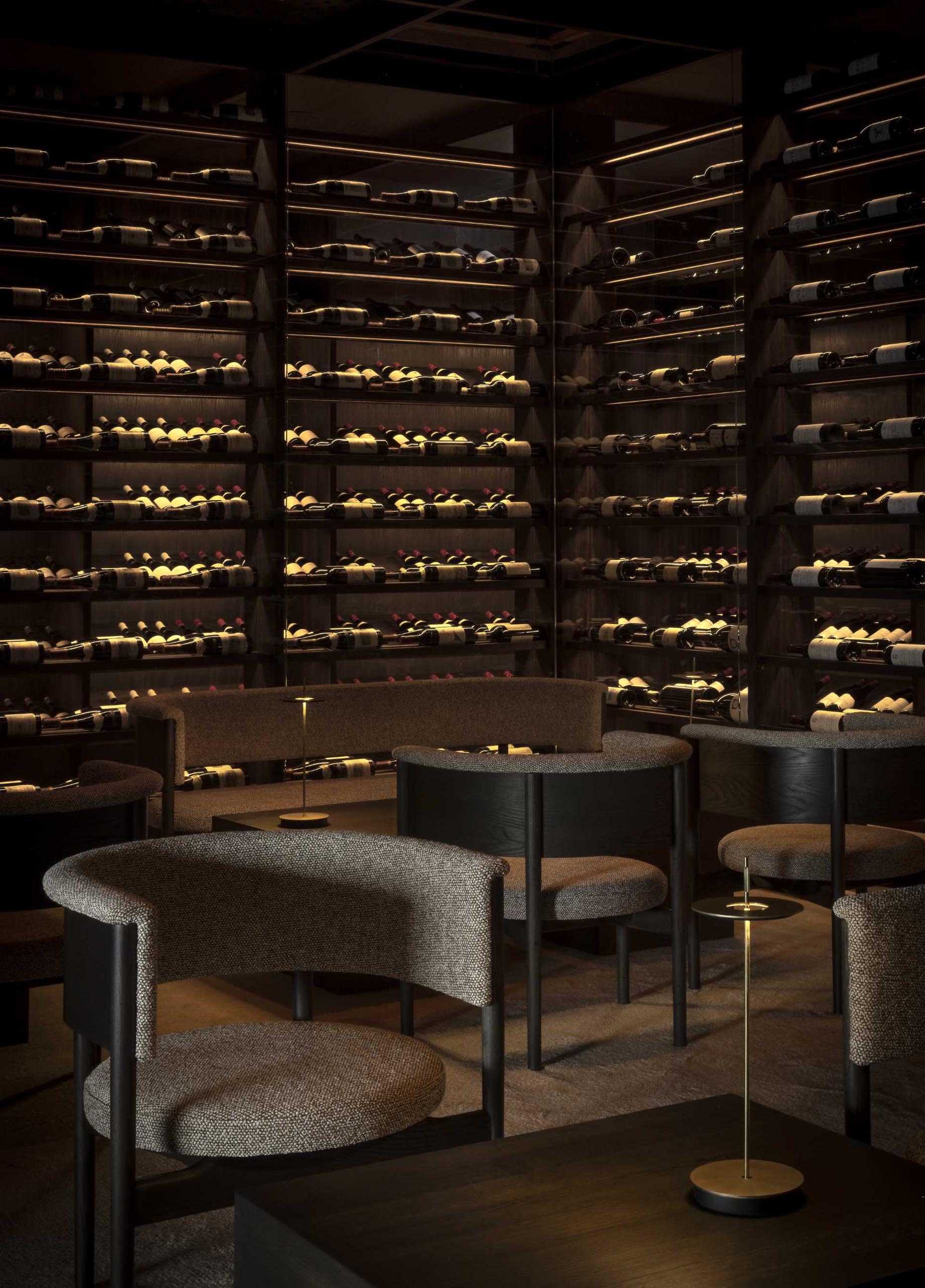 A dark and moody wine cellar with dark wood shelves and comfortable chairs.