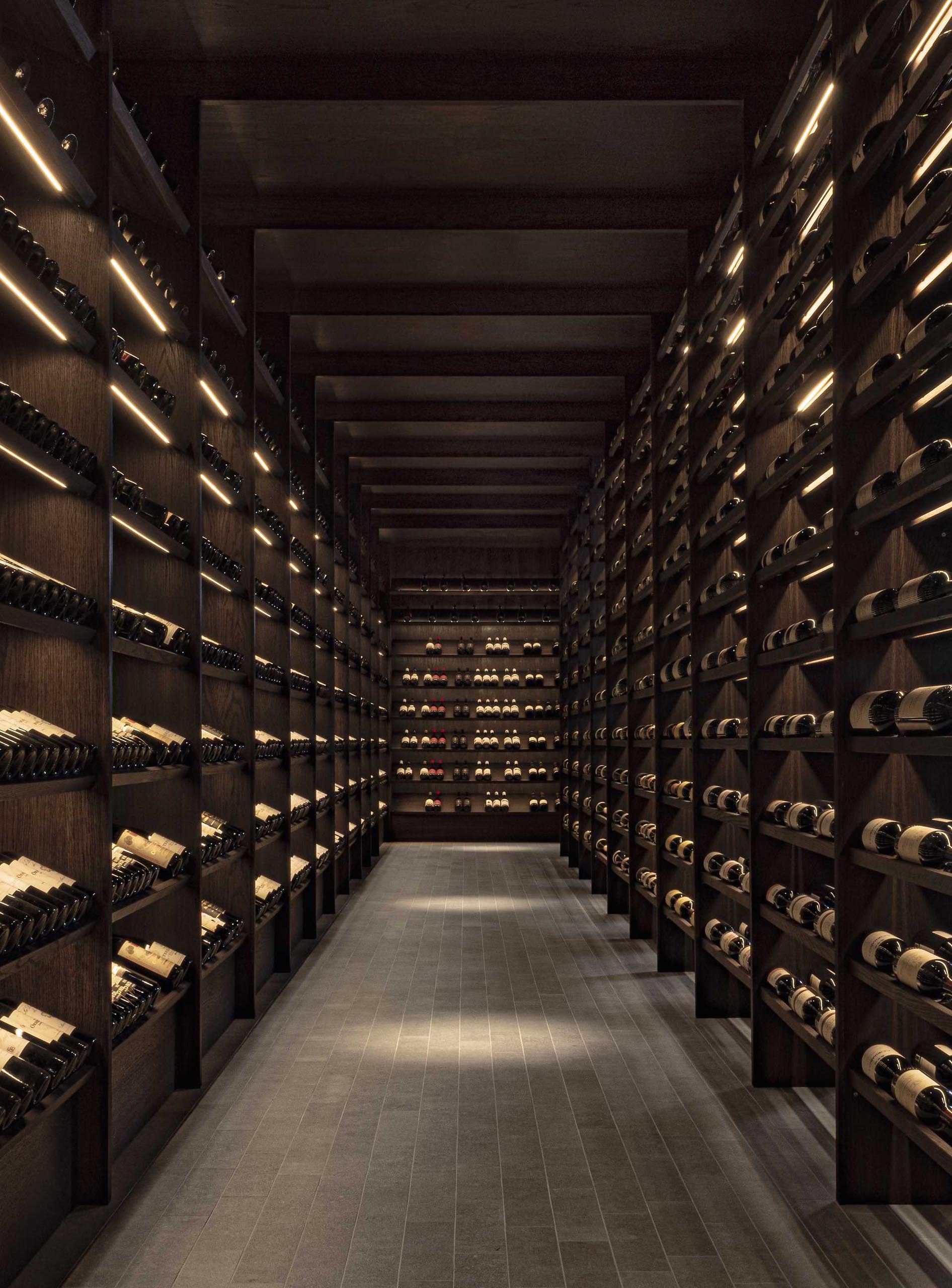 A dark and moody wine cellar with dark wood shelves.