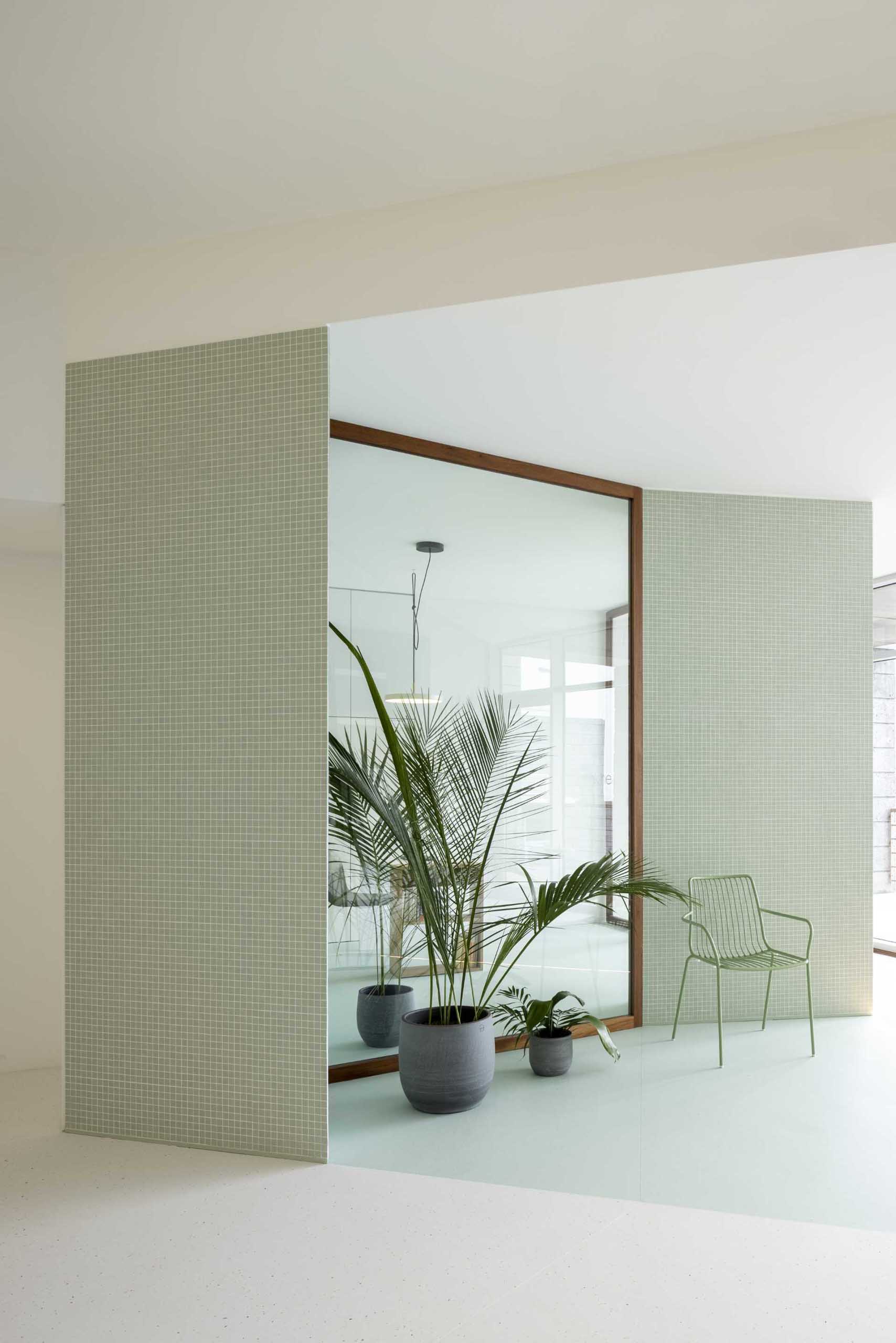 Small square pastel green tiles, as well as the flooring define the office area, and are complemented by plants and matching furniture.