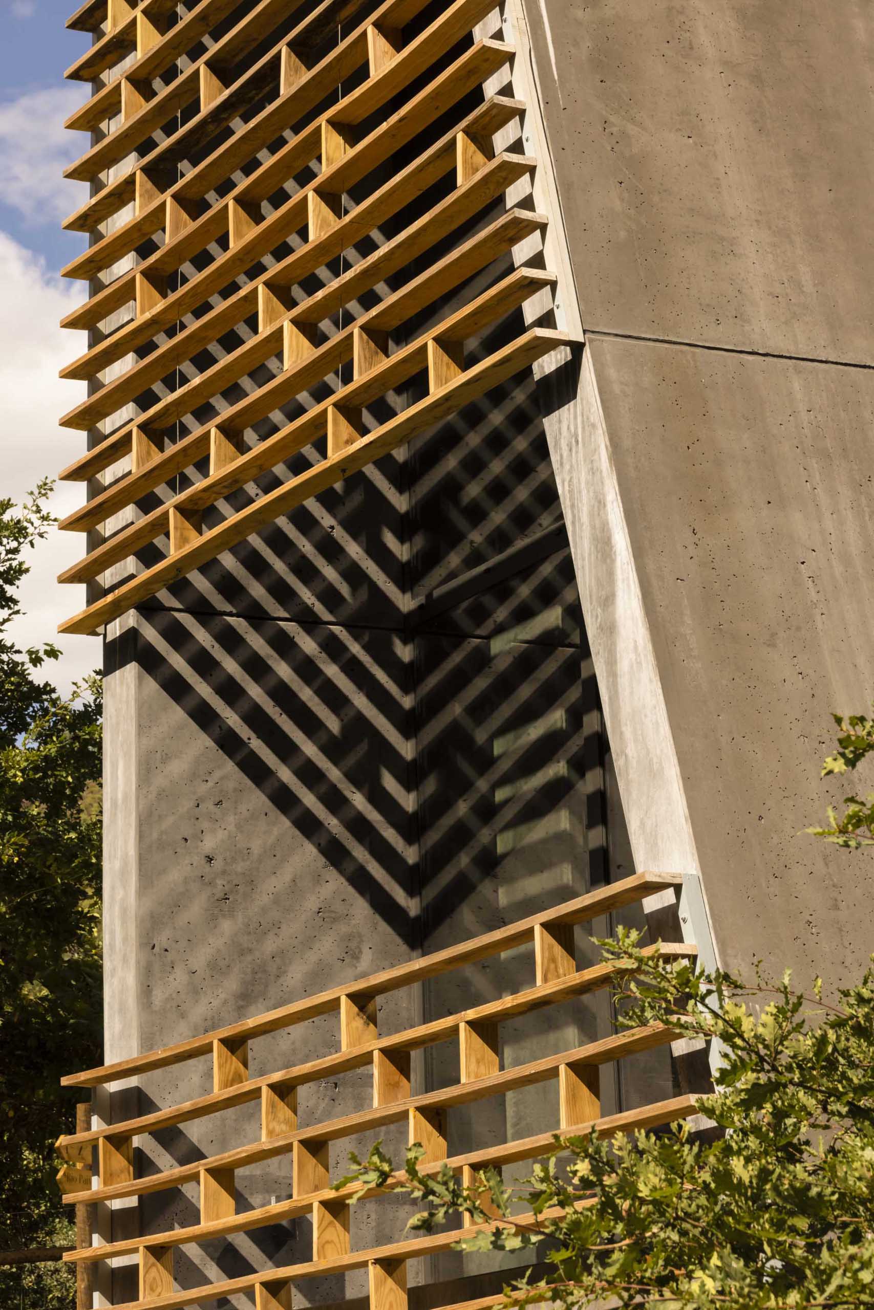 A small and modern cabin that's made from concrete and wood, and has a balcony.