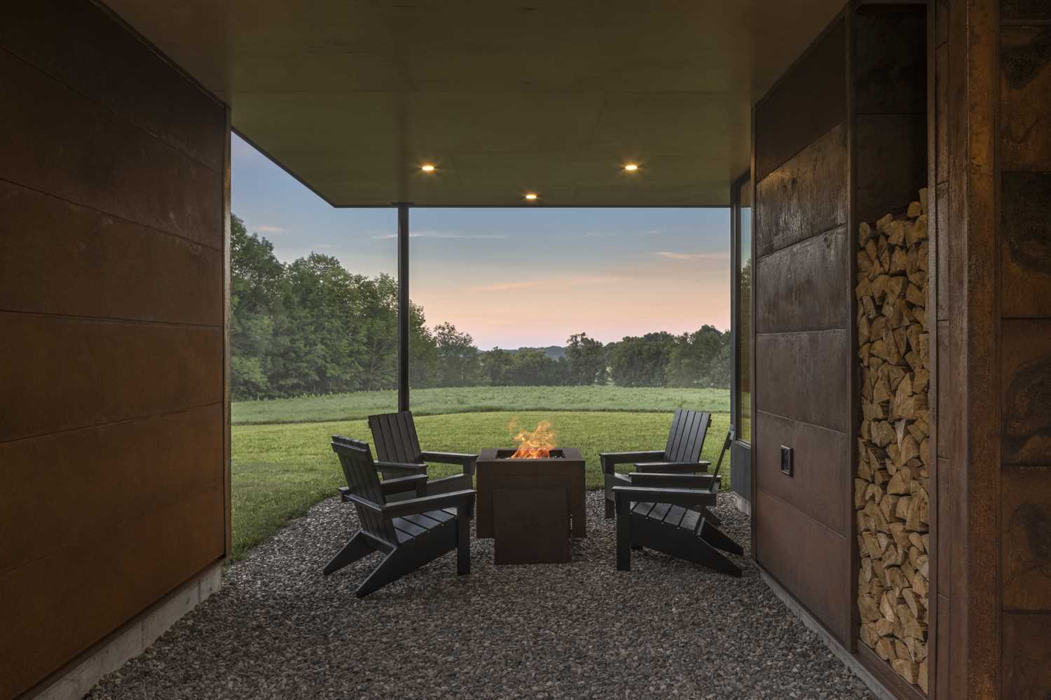 A covered outdoor patio, located between the main house and an art studio, includes a firepit surrounded by chairs.