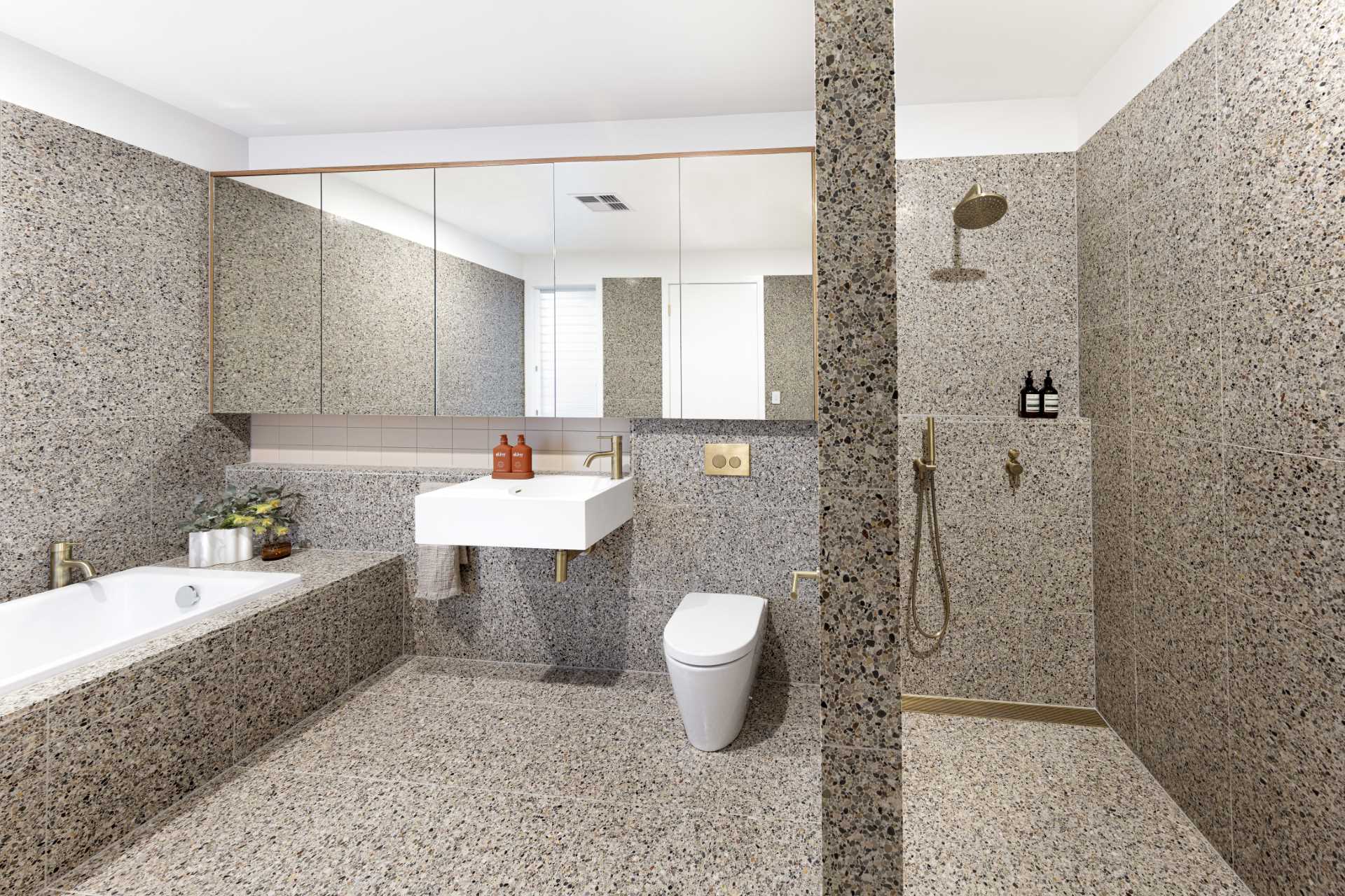 In this primary bathroom, tiles cover the walls and floor, while a built-in bathtub lines the wall and the shower is located behind a solid wall.