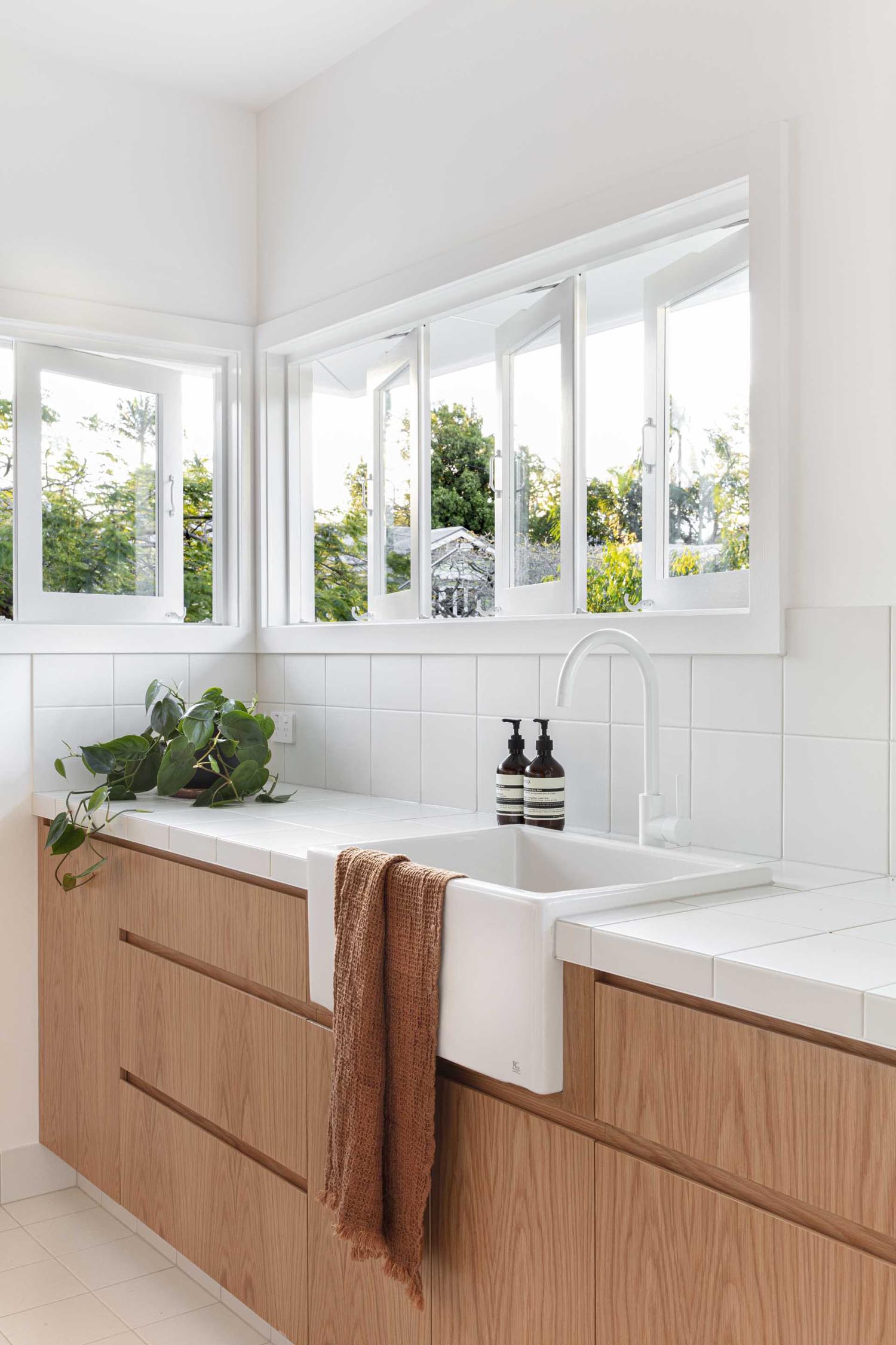 In this laundry room, hardware-free wood cabinets have been combined with a white apron sink, a white tiled countertop, and matching backsplash.
