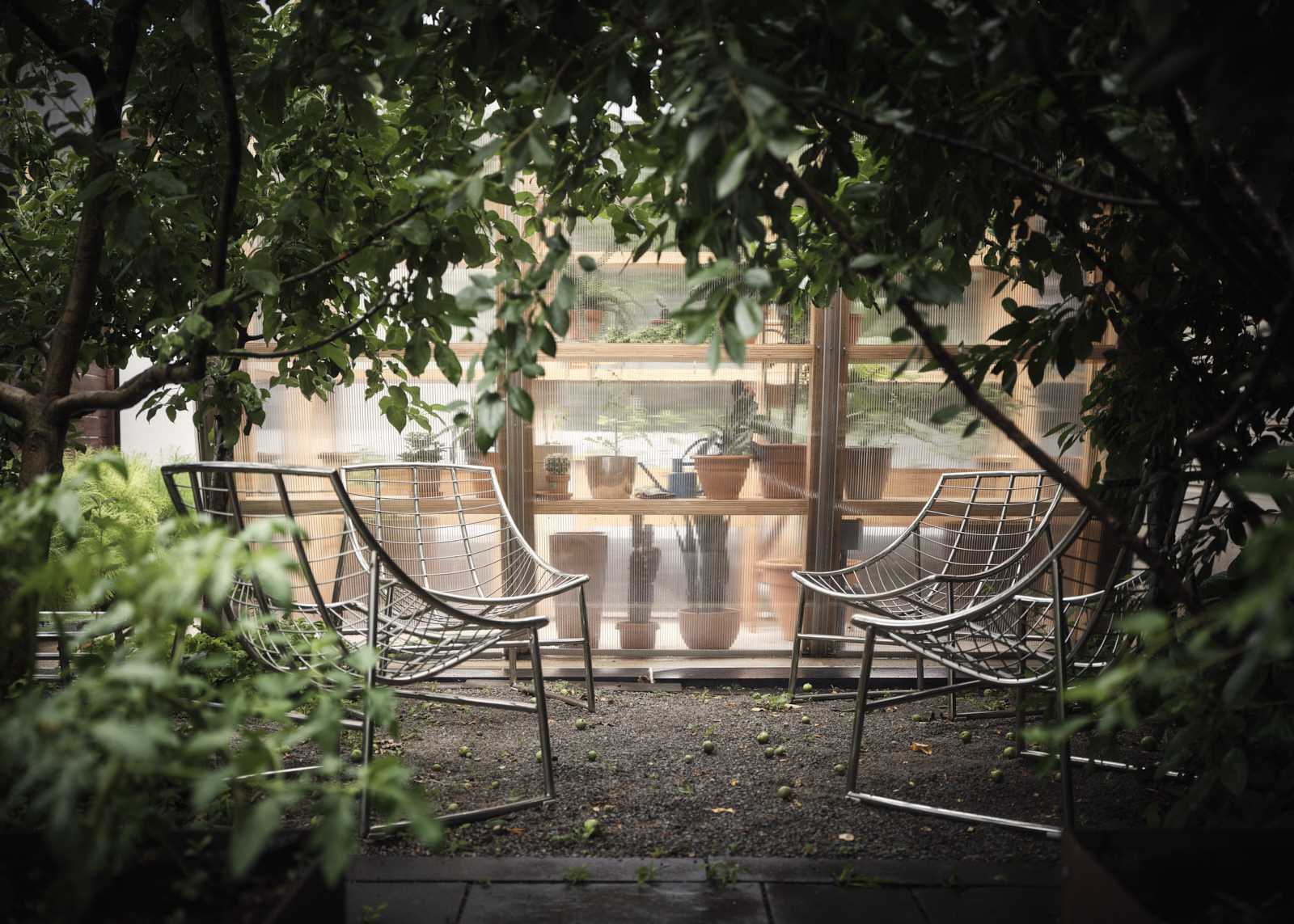 A modern and modular greenhouse in a backyard with a small seating area.