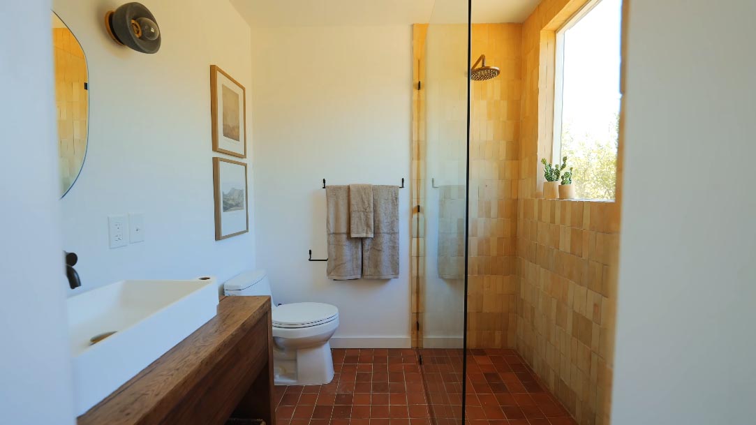 A tiny home made from a shipping container includes a modern bathroom with square tiles and a window.