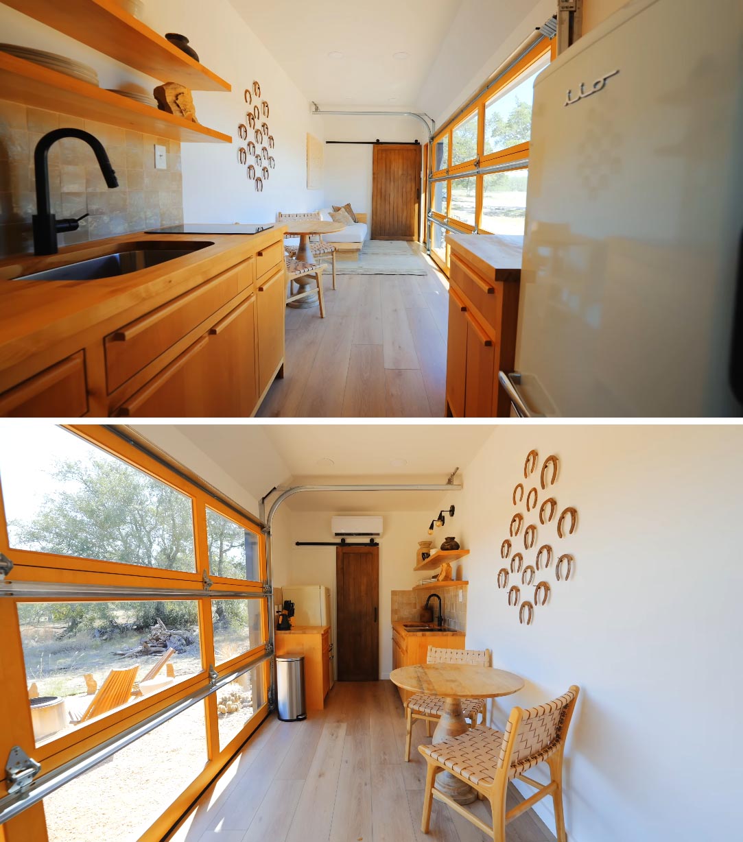 A tiny home made from a shipping container includes a main room with the living area, dining area, and kitchen with custom cabinets. A garage door can be opened to connect the living space with the outdoors.