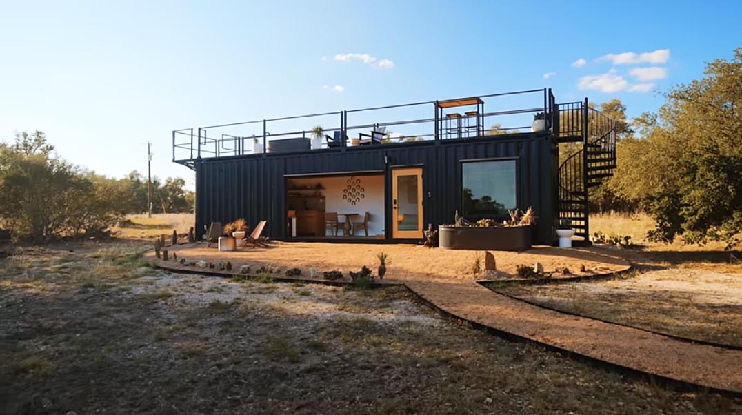 A modern tiny home made from a 40 foot shipping container, and has a garage door and a rooftop deck.