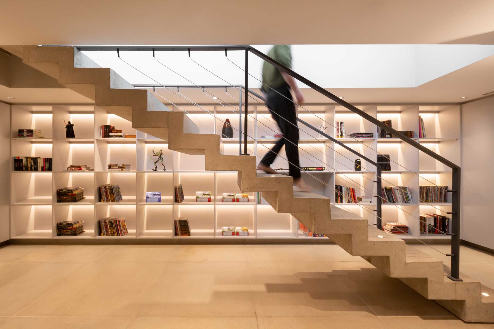 Concrete stairs lead down to a basement that has a wall of shelving with hidden lighting.