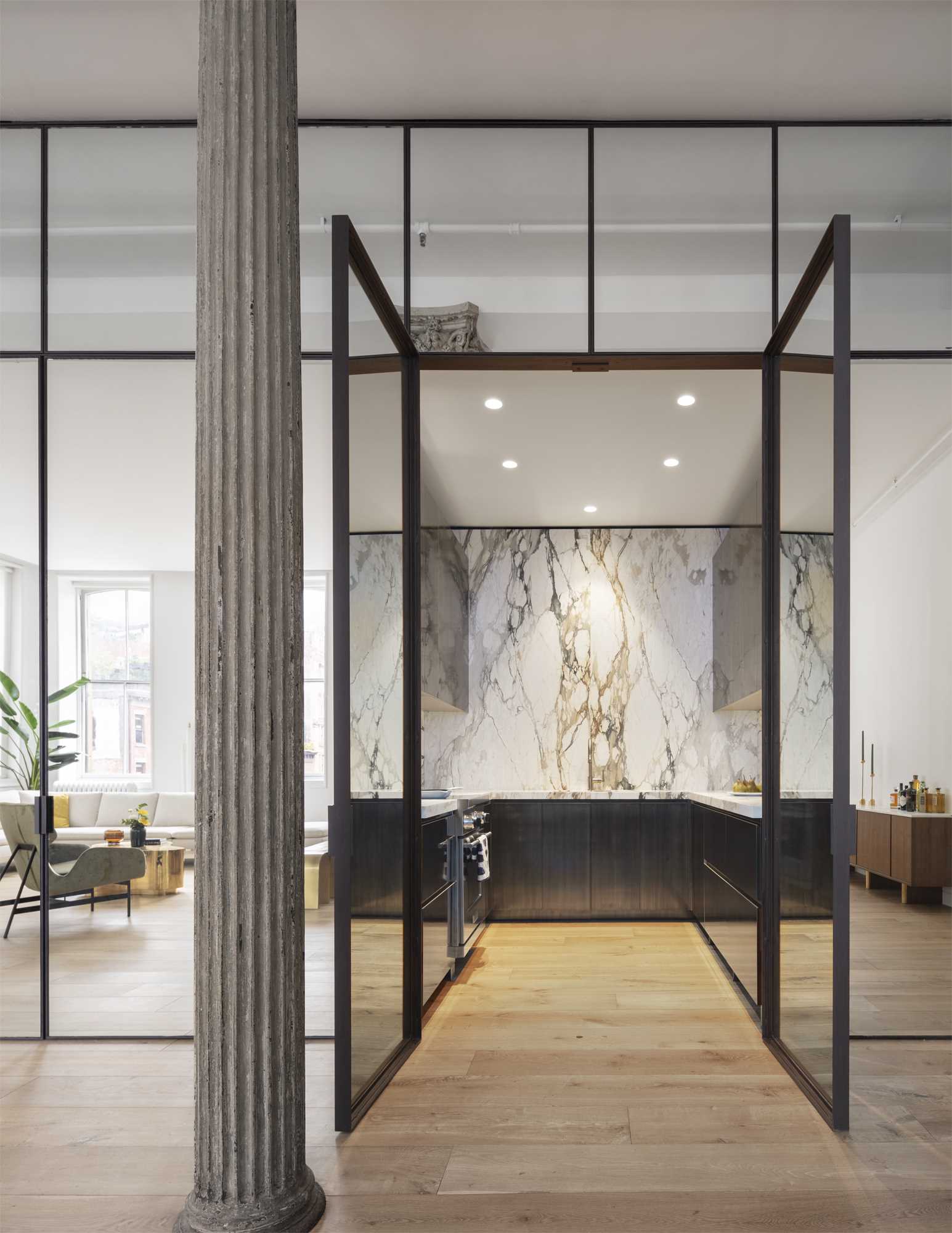 A mirrored set of doors opens into the kitchen where matte figurative marble and patinated brass millwork play off of the loft’s new wide-plank oak floors.