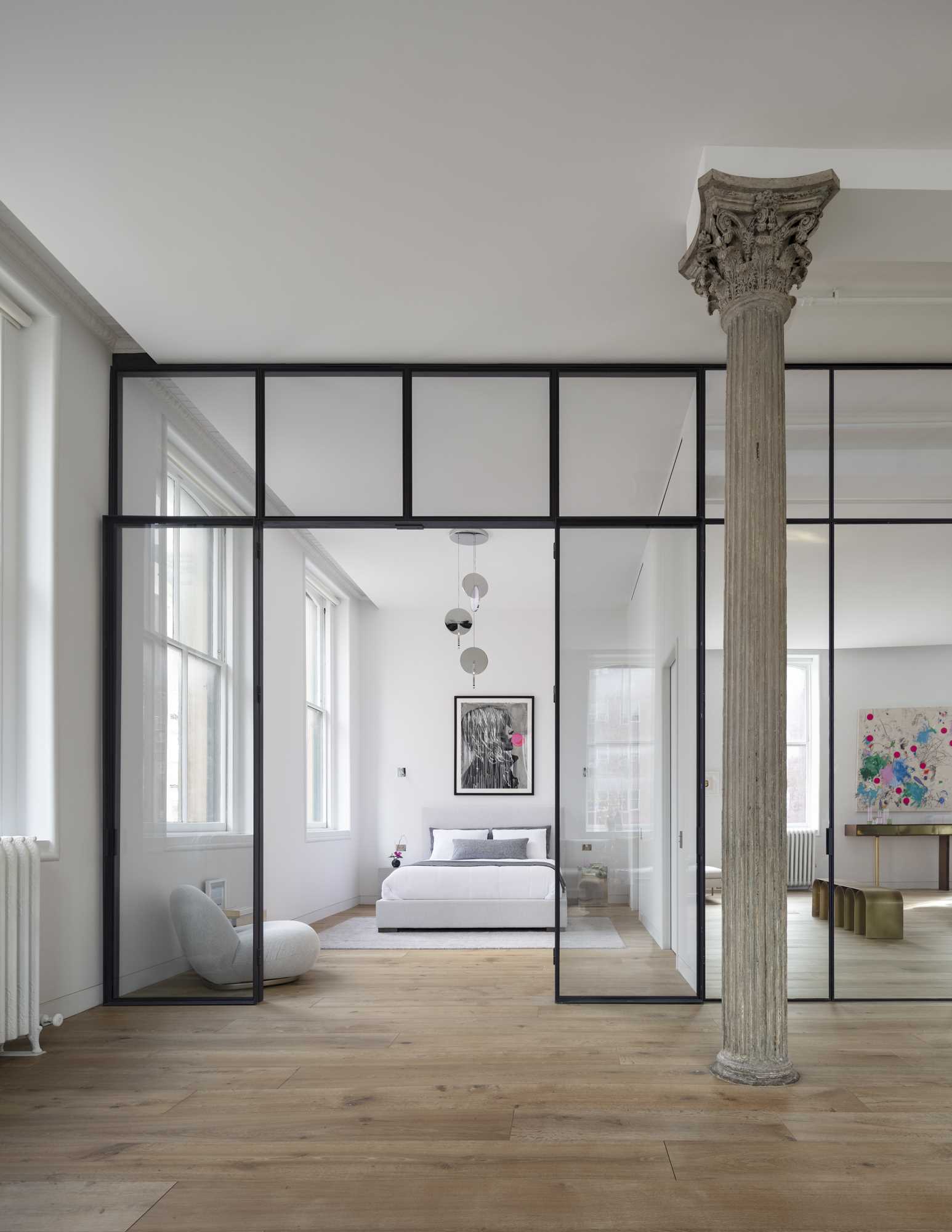 This modern bedroom, located by the windows, includes an Eclipse Chandelier by Lee Broom, a Pacha Lounge Chair by Pierre Paulin, and a Bubble Gum Girl Painting by Hijack.