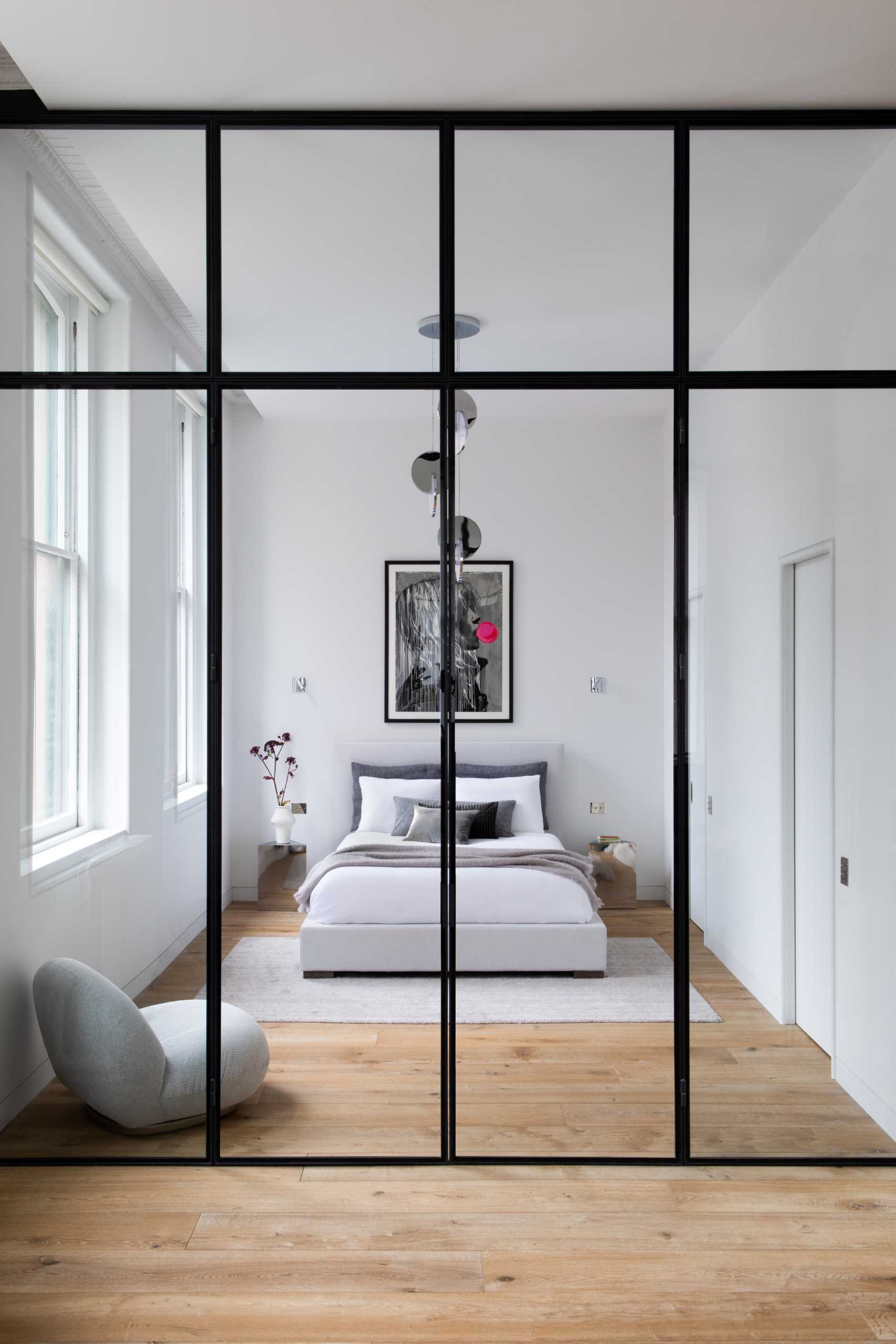 This modern bedroom, located by the windows, includes an Eclipse Chandelier by Lee Broom, a Pacha Lounge Chair by Pierre Paulin, and a Bubble Gum Girl Painting by Hijack.
