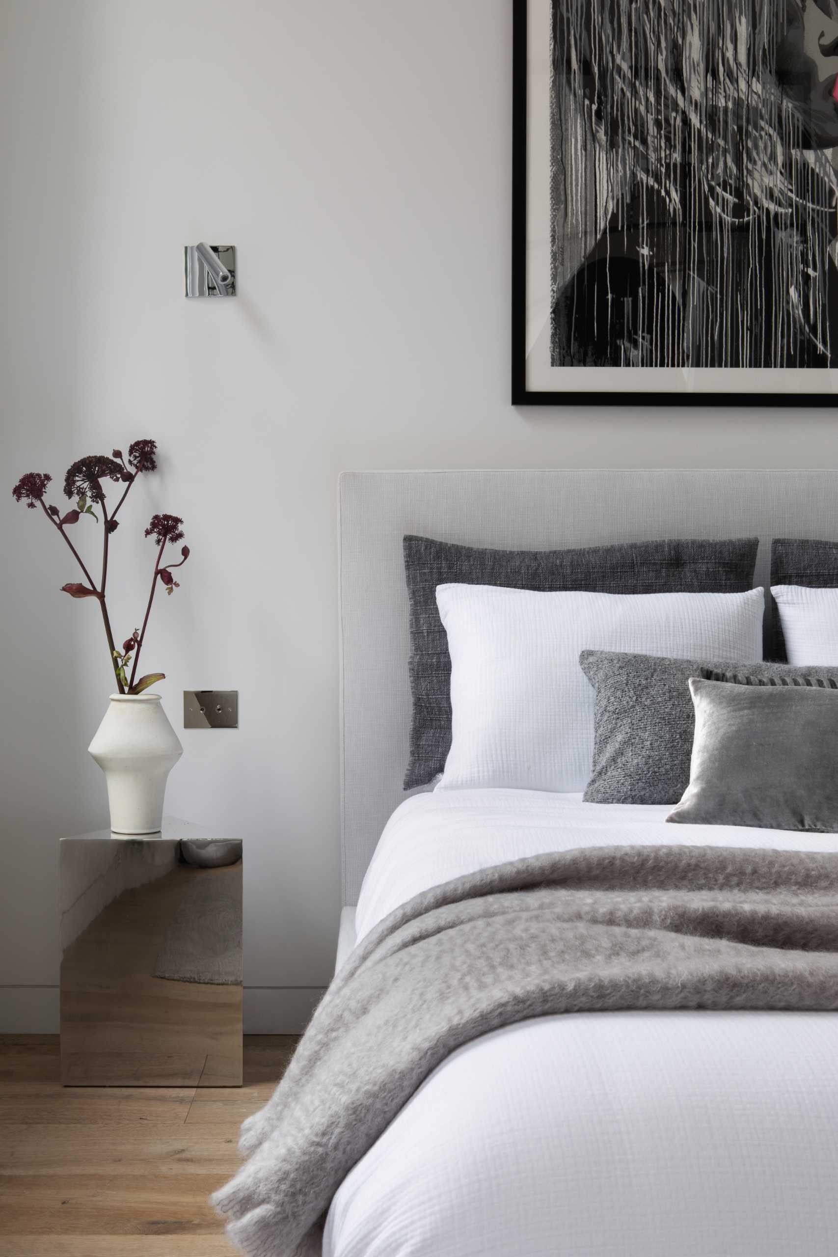 This modern bedroom, located by the windows, includes an Eclipse Chandelier by Lee Broom, a Pacha Lounge Chair by Pierre Paulin, and a Bubble Gum Girl Painting by Hijack.