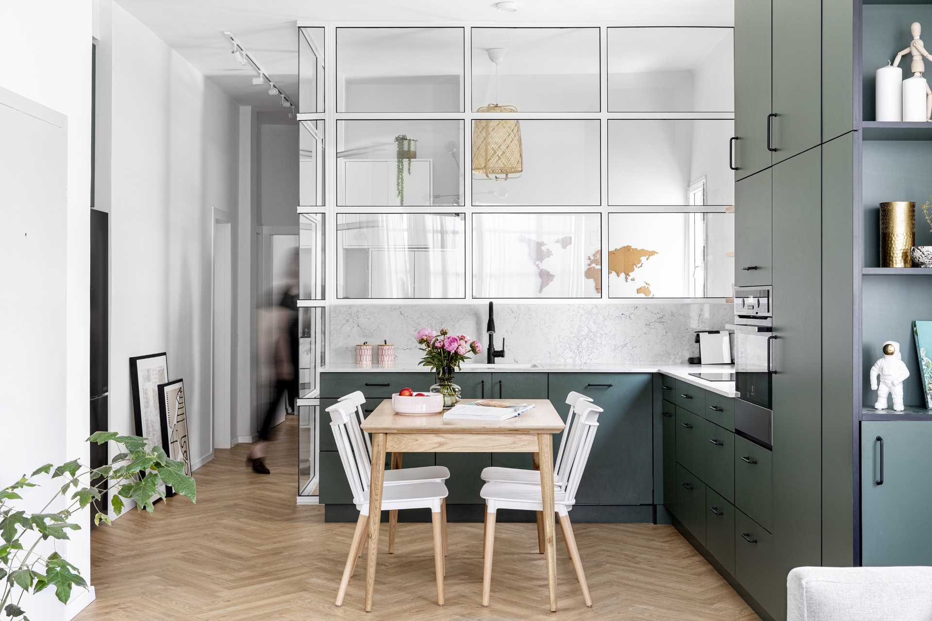A modern apartment with a dark green kitchen and a glass-enclosed home office.