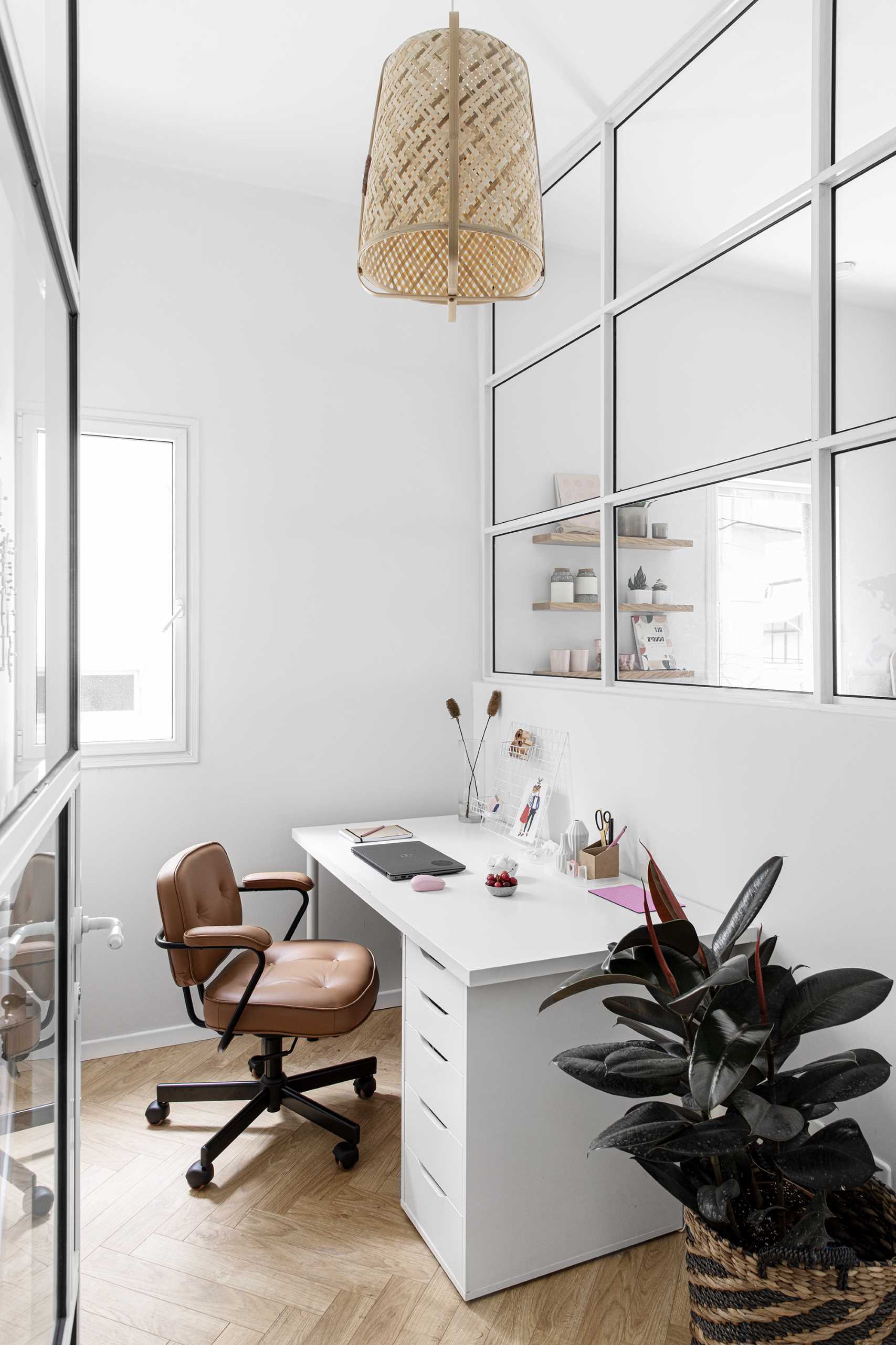 Inside this glass-enclosed home office, there's a desk against the wall, while on the opposite wall, there's a wood world map and storage.