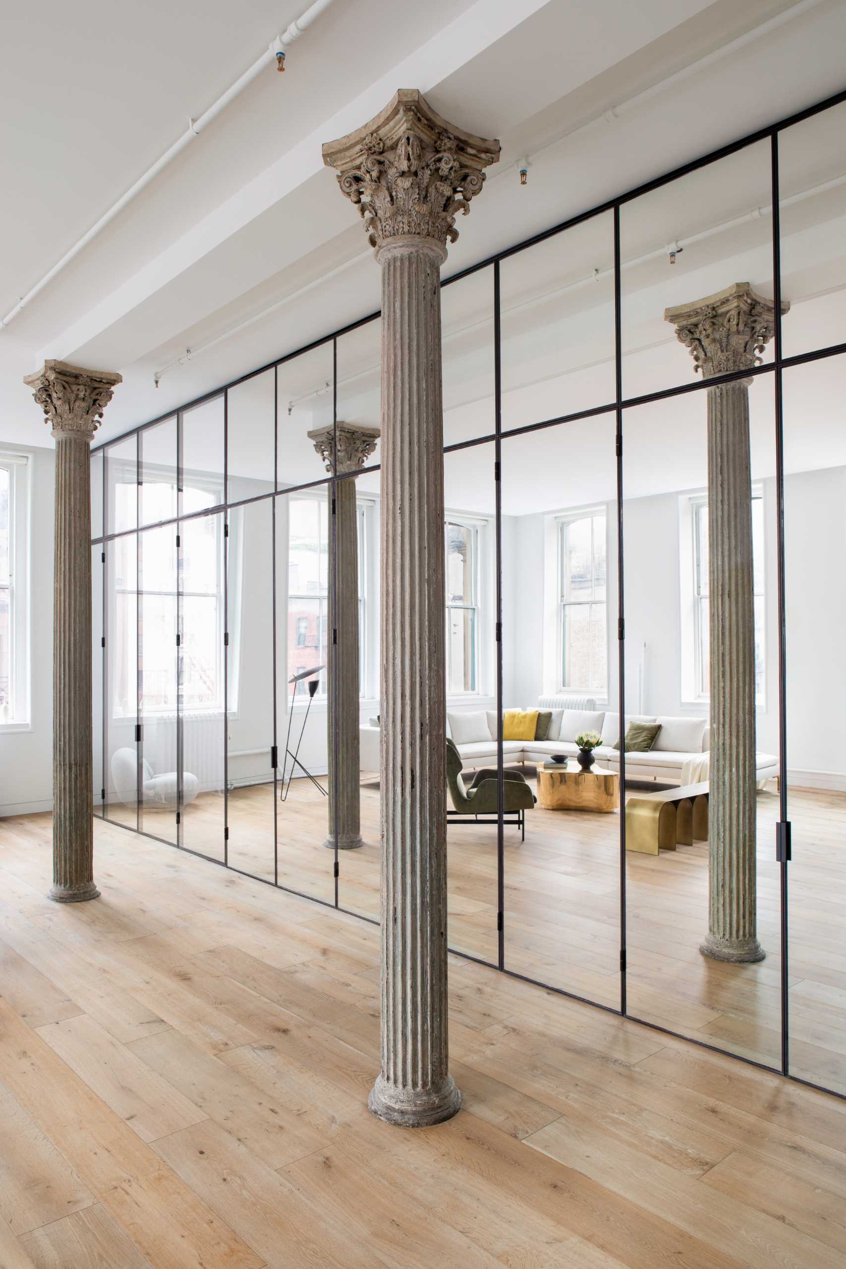 Key to the design of this updated loft apartment, is a wall of floor-to-ceiling, black-framed glass that includes a combination of clear glass and mirrored panels. 