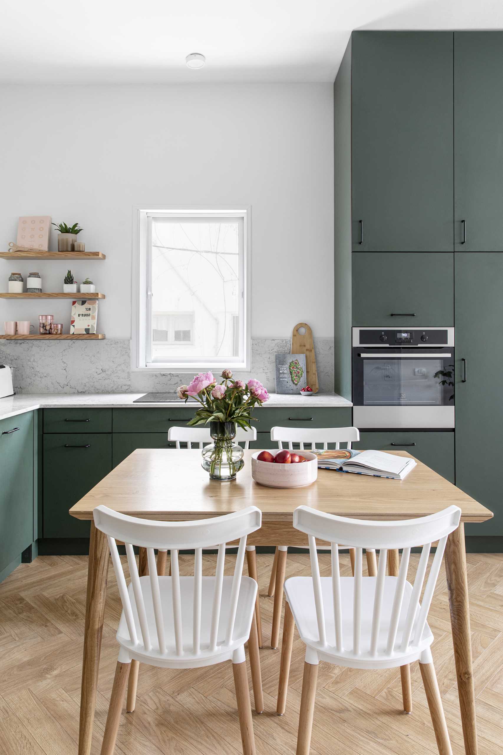 The kitchen and dining room are combined, with the dark green cabinets adding color and complementing the plants in the living room.