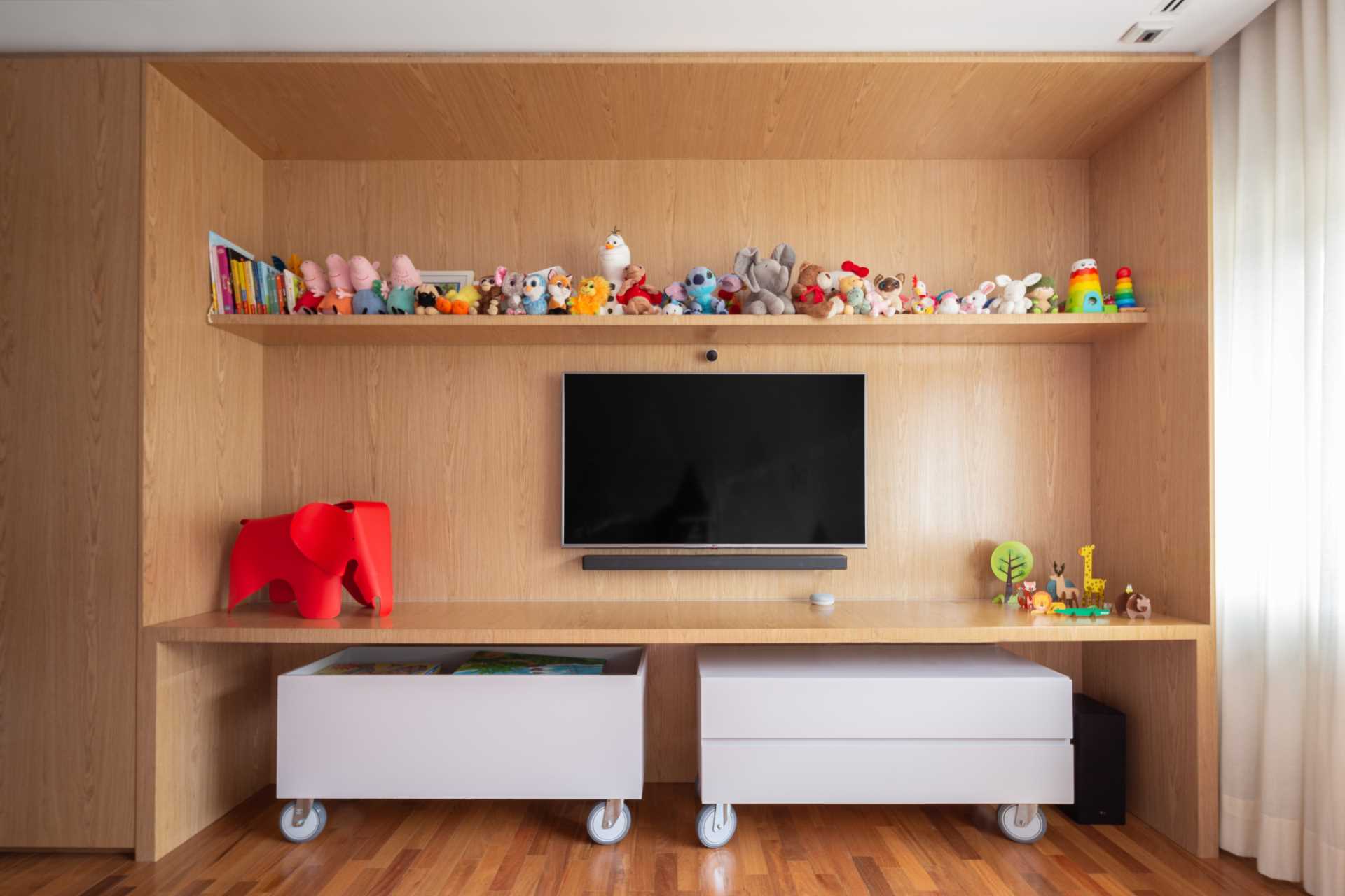 A wood accent wall in a kids bedroom has a shelf for toys, and storage bins on wheels underneath.