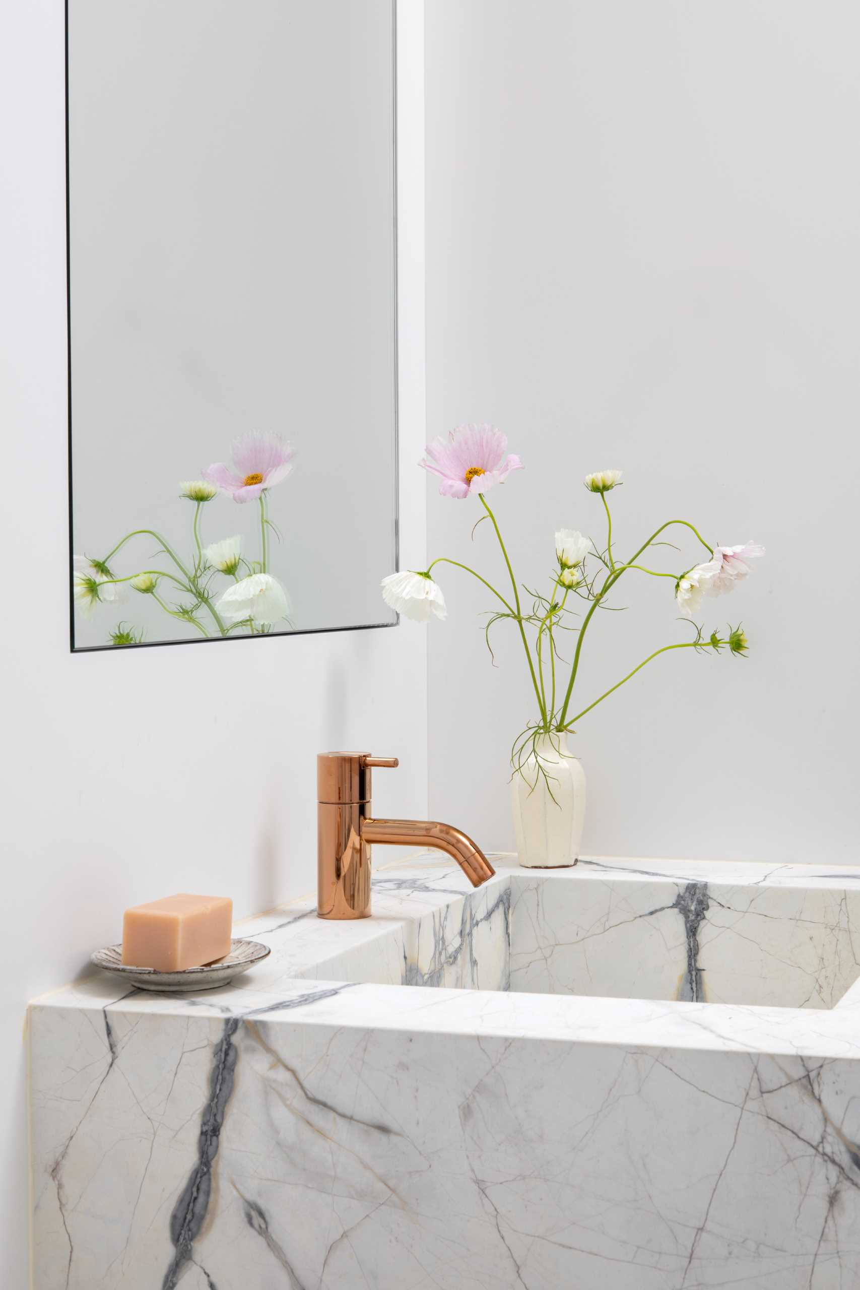 A modern bathroom that's enveloped in veined marble with accents of bright metallics.