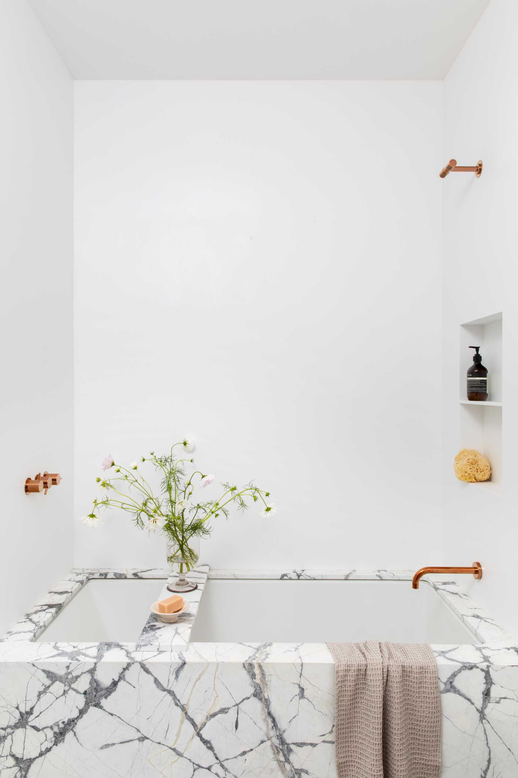 A modern bathroom that's enveloped in veined marble with accents of bright metallics.