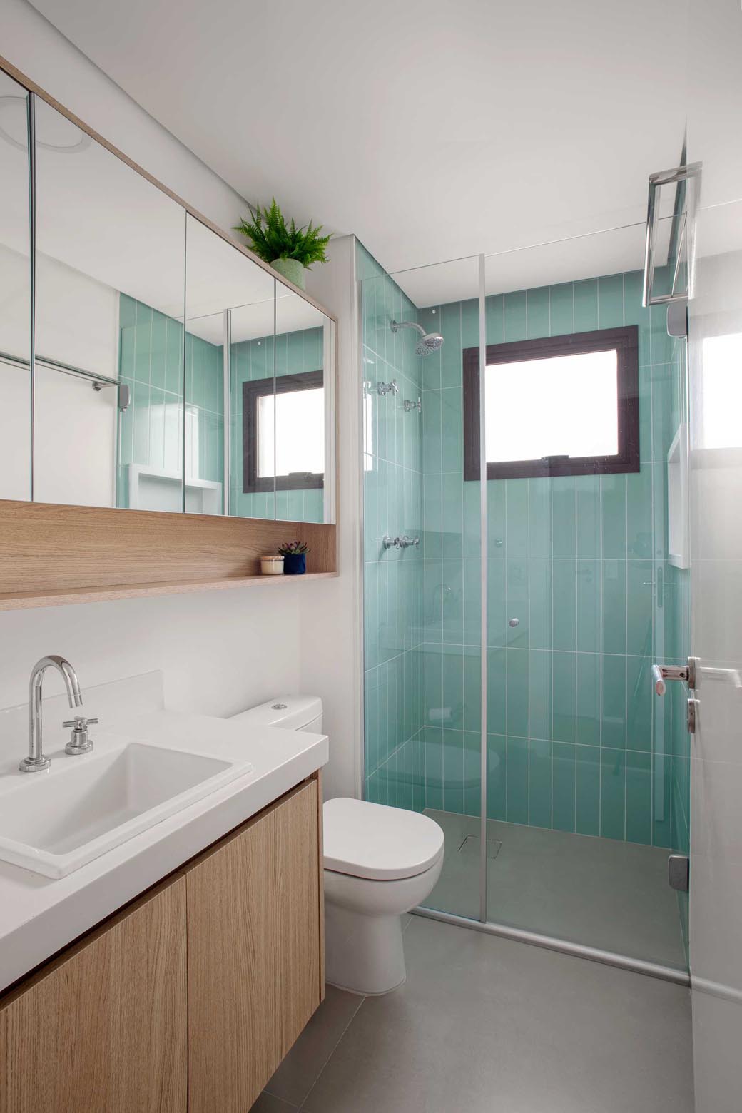 In this bathroom, the shower is lined with light turquoise tiles, while the wood vanity and shelf add a natural element.